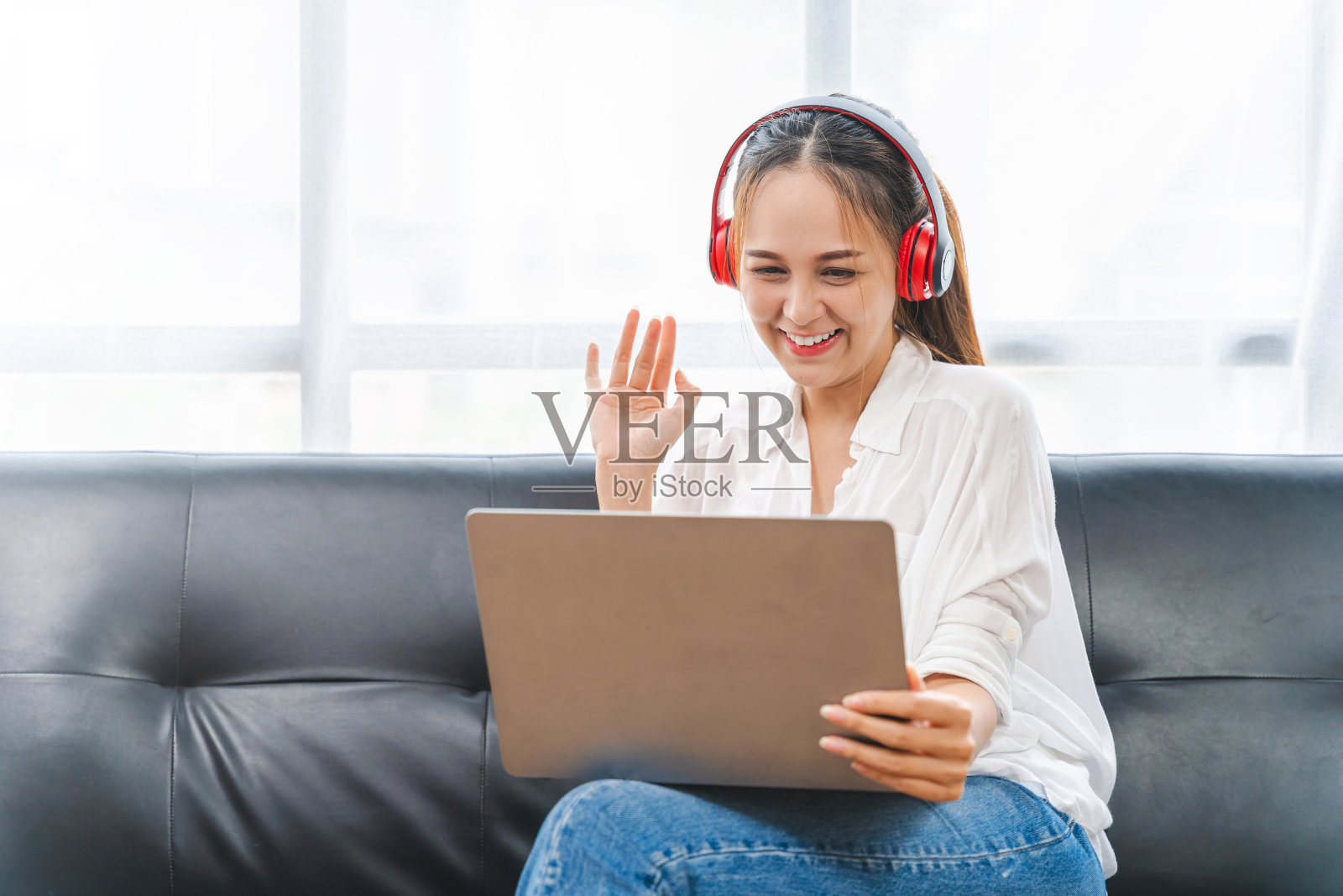 年轻的商业自由职业亚洲女性坐在沙发上用笔记本电脑查看社交媒体新闻。说嗨，挥手。照片摄影图片