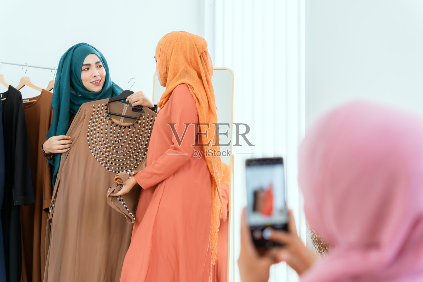一群穆斯林女性朋友用手机拍视频，朋友们用手机买衣服。照片摄影图片