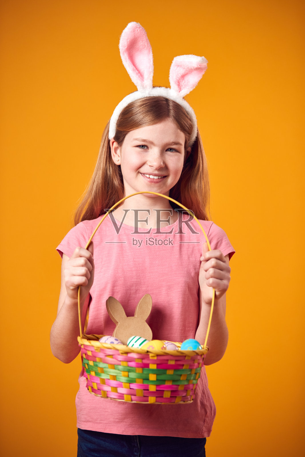 工作室拍摄的女孩戴着兔子耳朵和手持复活节彩蛋篮子在黄色背景照片摄影图片