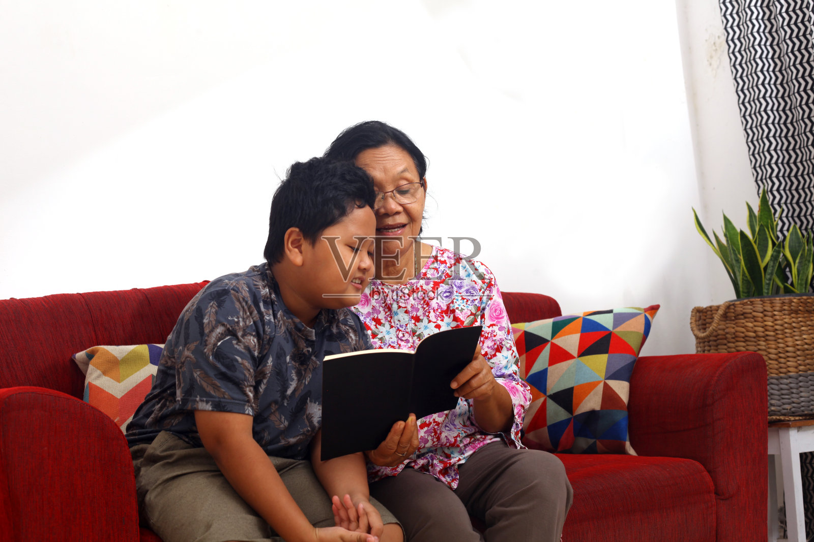 年轻的亚洲男孩和亚洲祖母在家里读书。侧视图与copyspace照片摄影图片