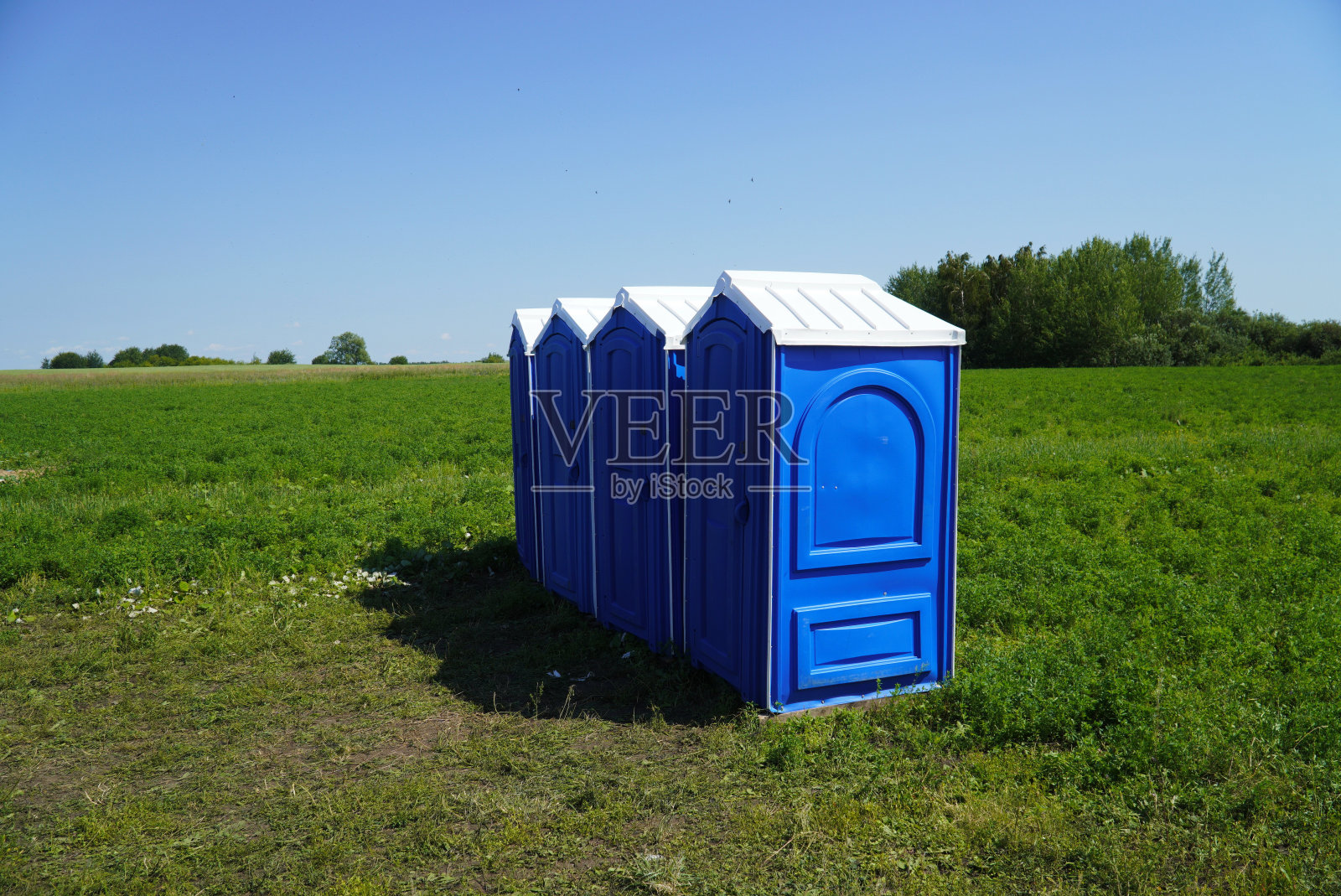 便携式塑料厕所在田野上的草地上，背景是蓝天。照片摄影图片
