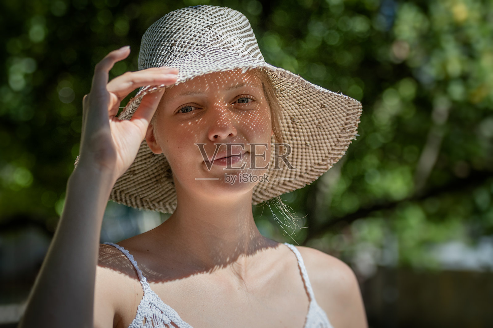 一幅浪漫的肖像，一个戴着帽子的白裙子的女孩在别墅的花园里度假。照片摄影图片