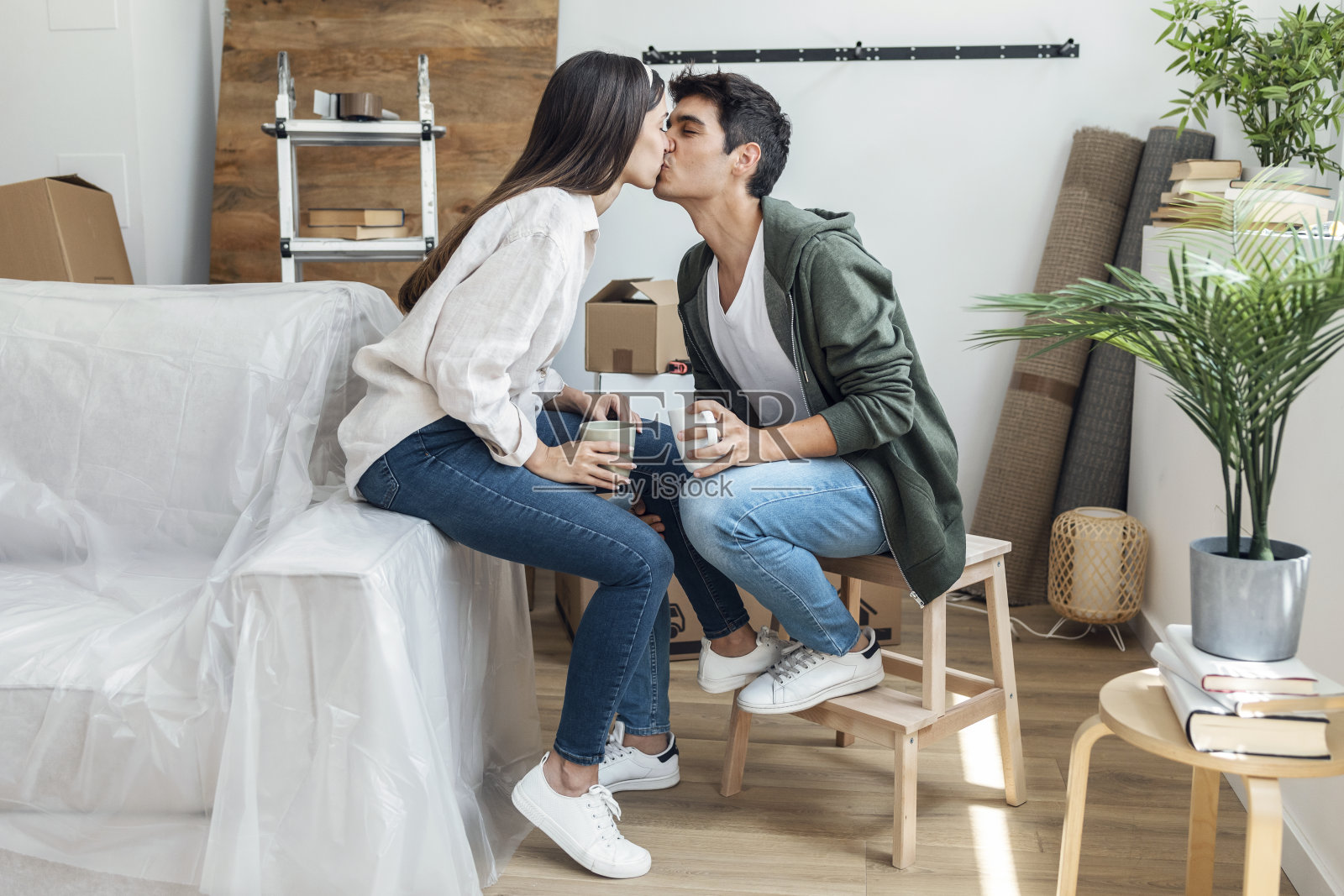 一对美丽的情侣在搬到他们的新房子的纸箱周围放松的时候接吻照片摄影图片