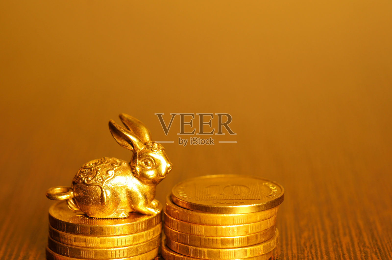 一个金属兔子雕像与硬币特写在一个金色的背景。照片摄影图片