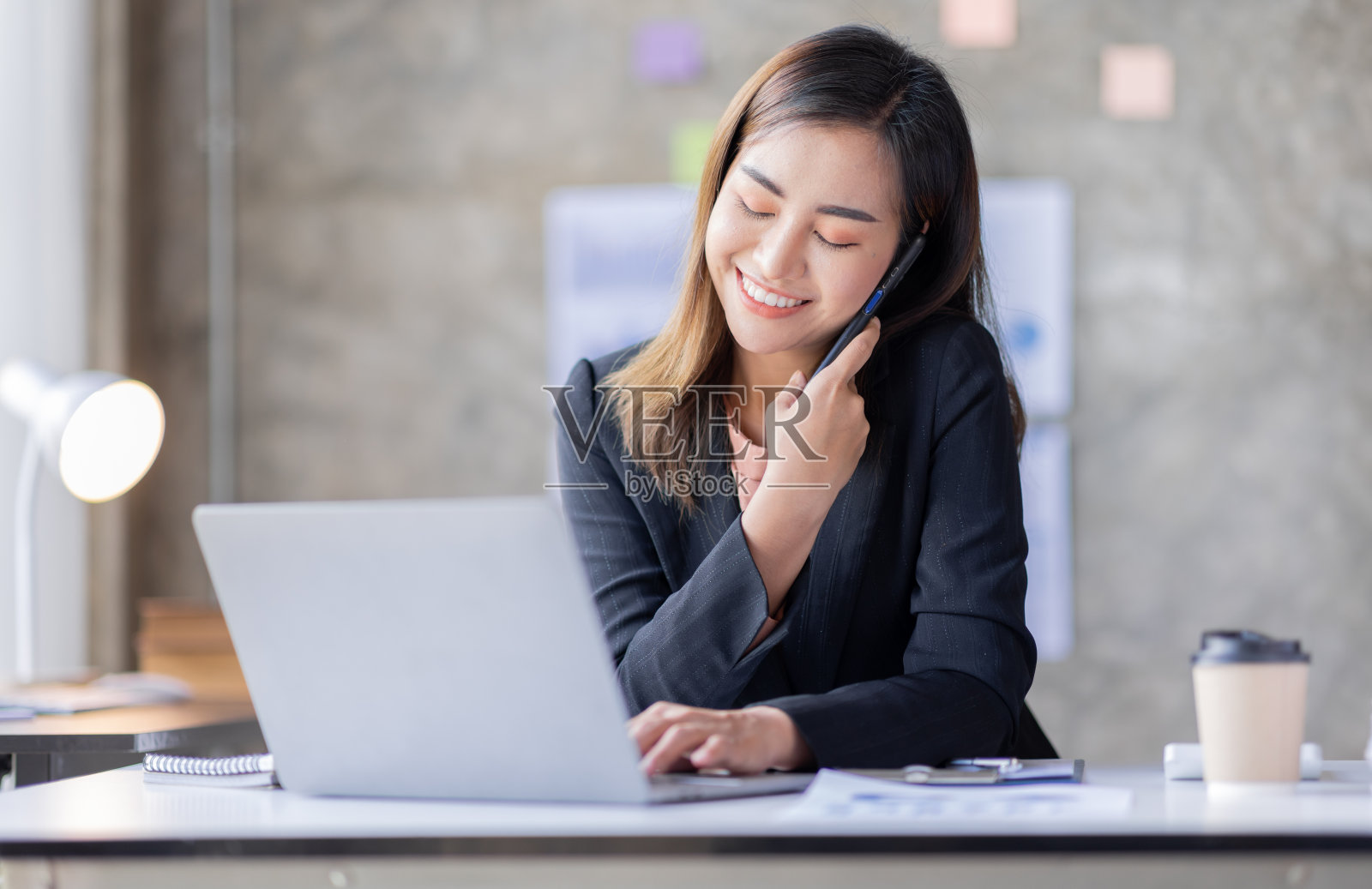 年轻的亚洲商业女性在办公室用智能手机聊天。坐在他工作场所的亚洲女性。照片摄影图片