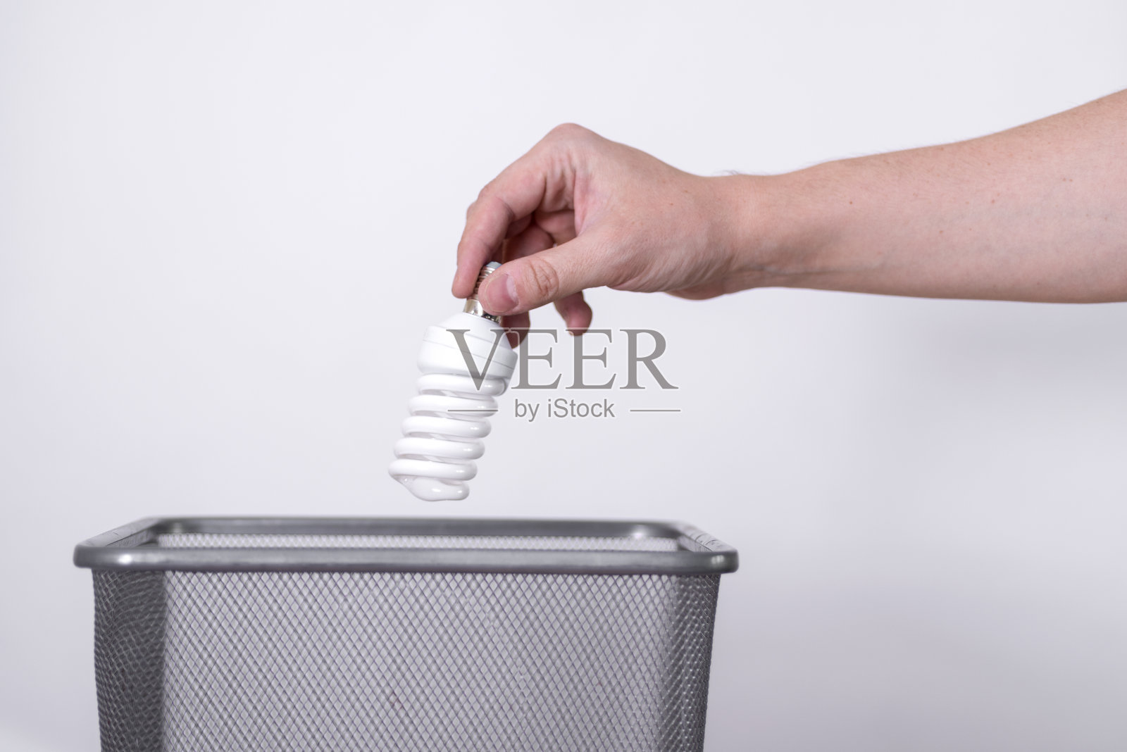 一只手把一个灯泡扔进灰色背景的垃圾桶里。照片摄影图片