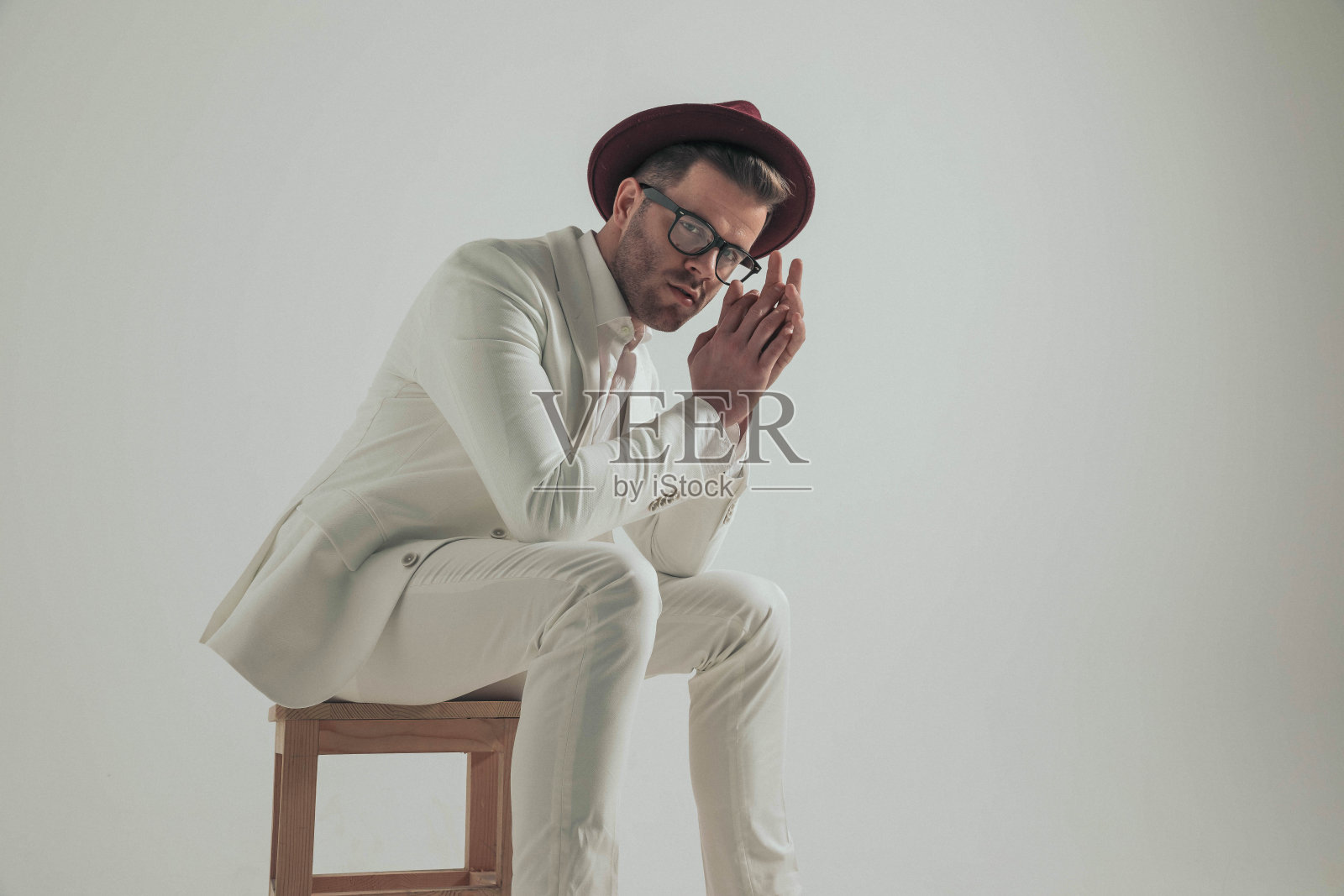 时髦的年轻人戴着帽子，穿着白色西装坐在木椅上照片摄影图片