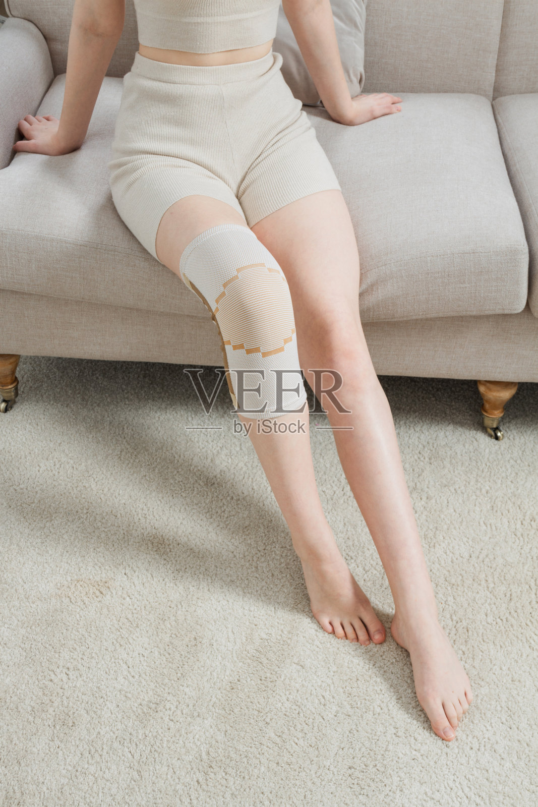 女人腿上的膝盖支撑支架。女孩戴着矫形器在屋子里。骨科解剖支架，用于膝关节固定、损伤和疼痛。膝关节绷带套筒。弹性运动照片摄影图片