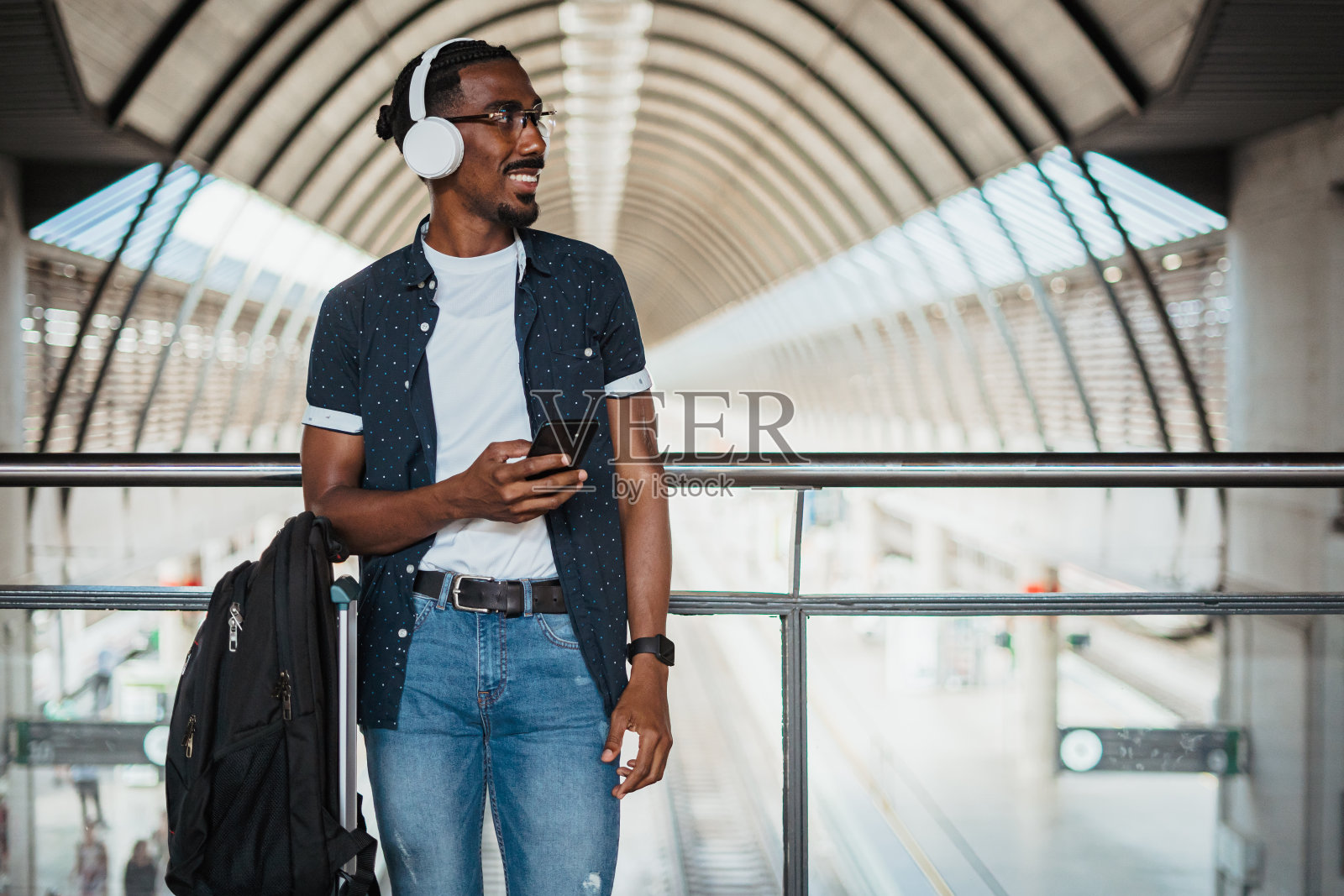 快乐的非洲人听音乐的无线耳机，而他在火车站等待照片摄影图片
