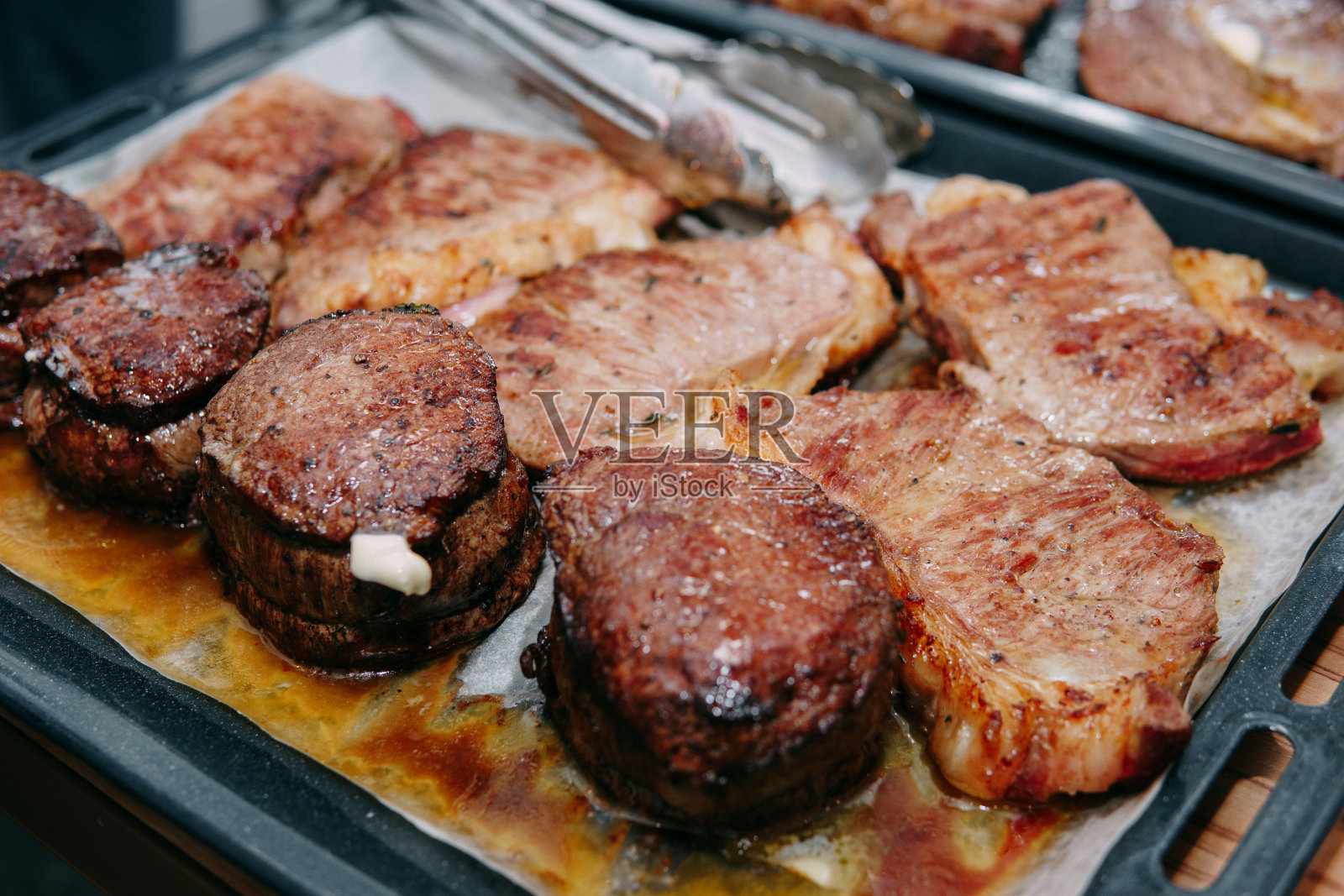 用平底锅煮牛排。在烹饪大师班做牛肉。戴着黑色手套的厨师的手。照片摄影图片