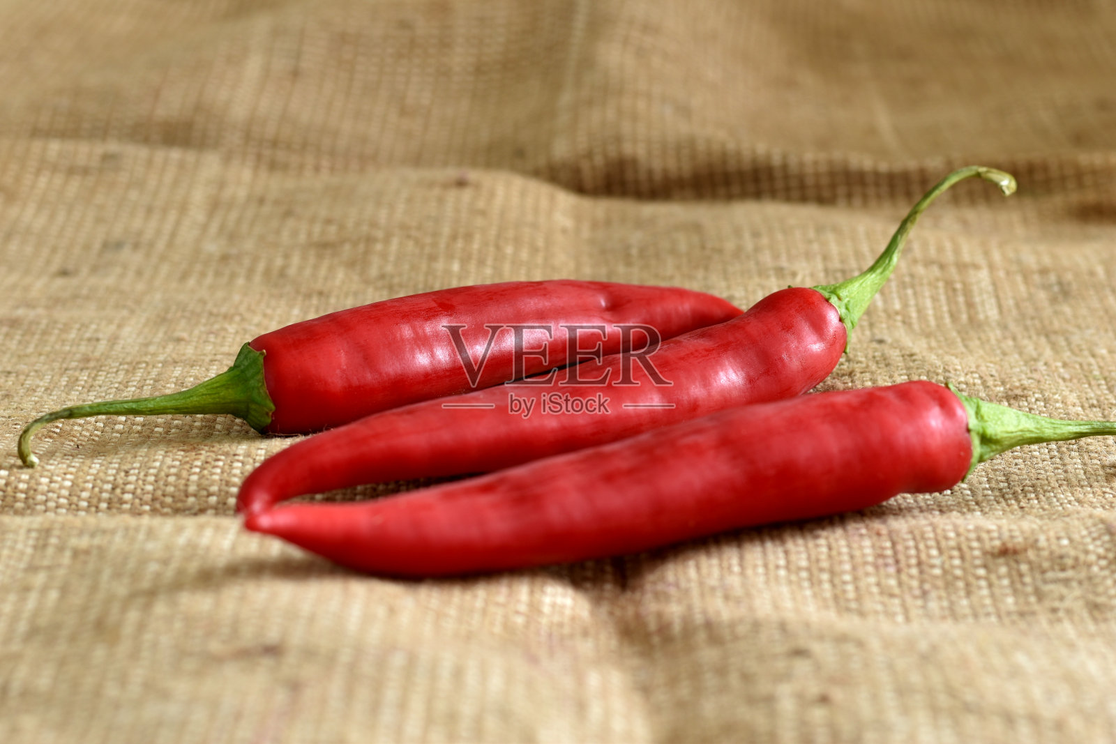 三个苦红辣椒躺在麻布上。照片摄影图片