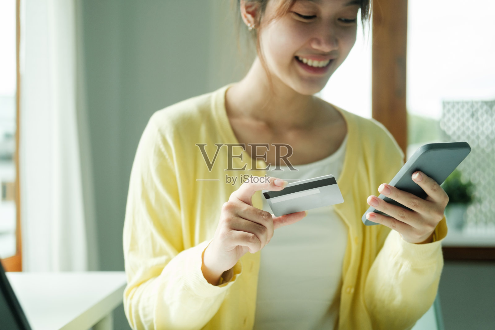 亚洲女性手里拿着信用卡，正在使用手机，智能手机。照片摄影图片