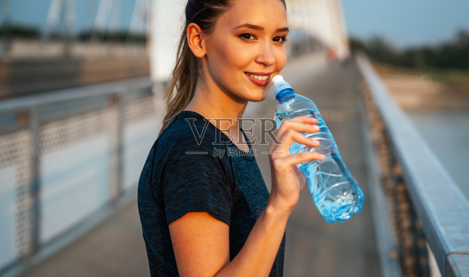 手持水瓶的健身女跑步者。健身女性在跑步锻炼后休息。照片摄影图片