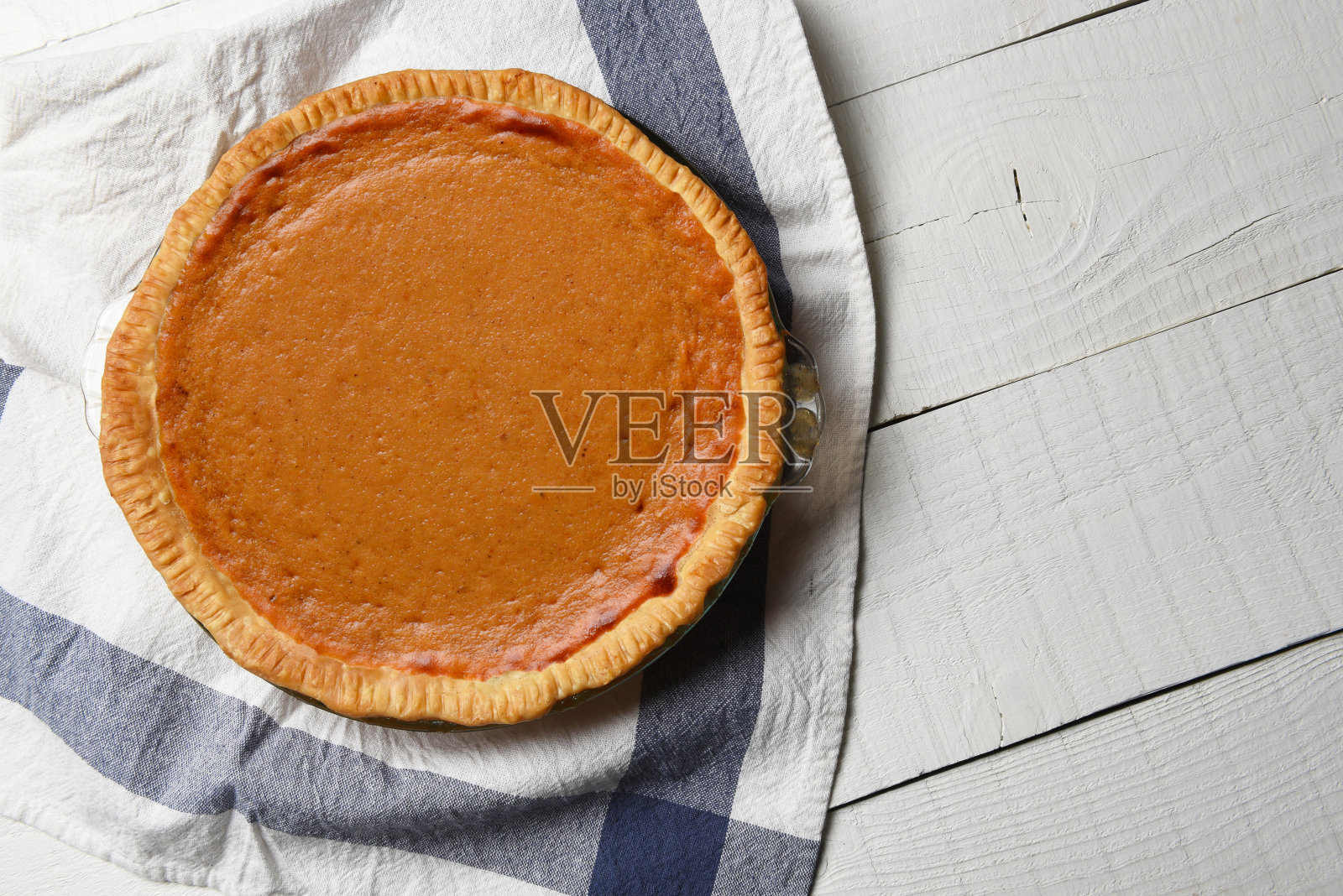 白色木桌上放着新鲜出炉的自制南瓜派和茶巾。高角度拍摄与拷贝空间。照片摄影图片