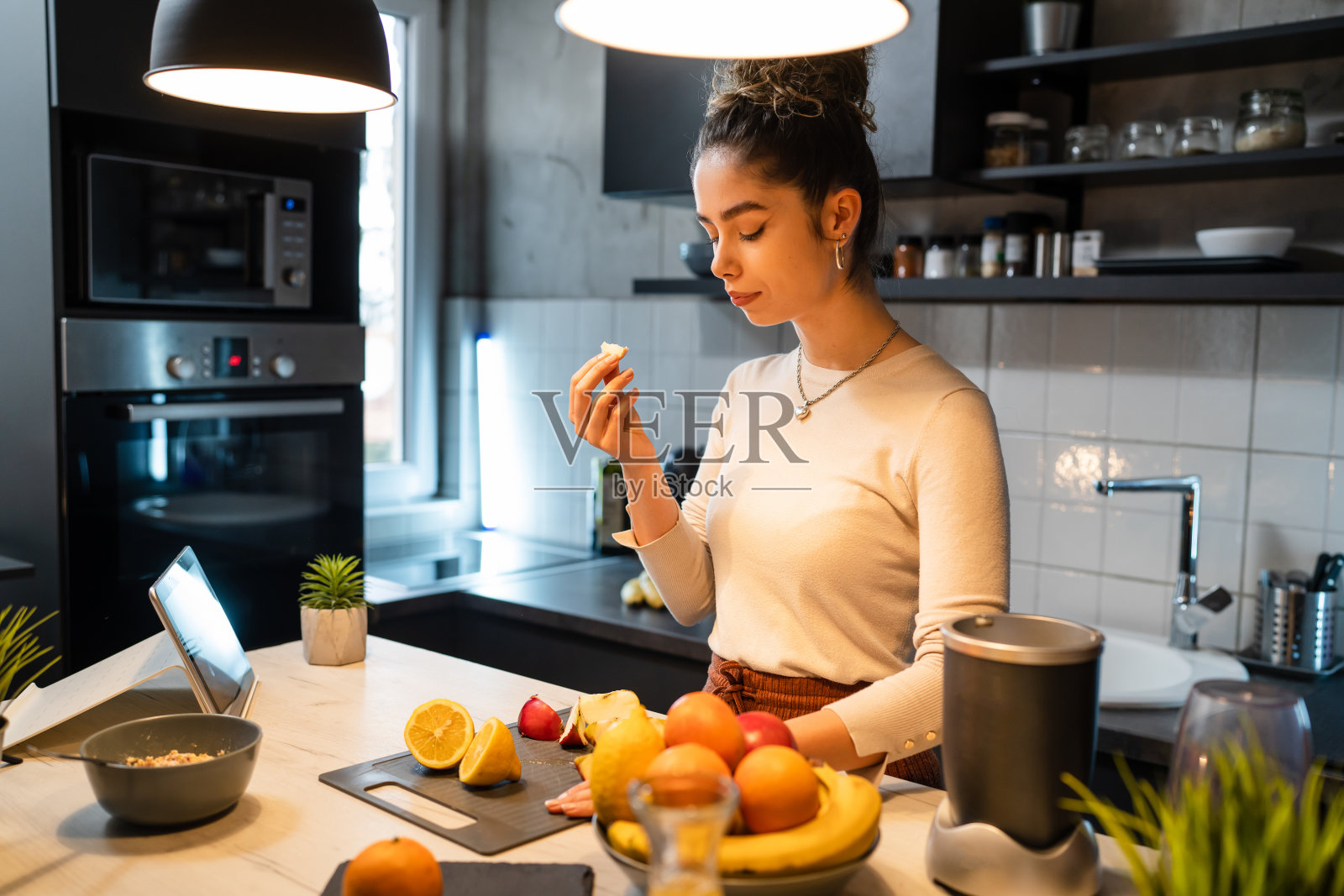 一个女人年轻的成年人快乐的白人女性微笑，而切割和吃水果在厨房柜台在早上健康饮食素食和素食的概念真实的人复制空间照片摄影图片