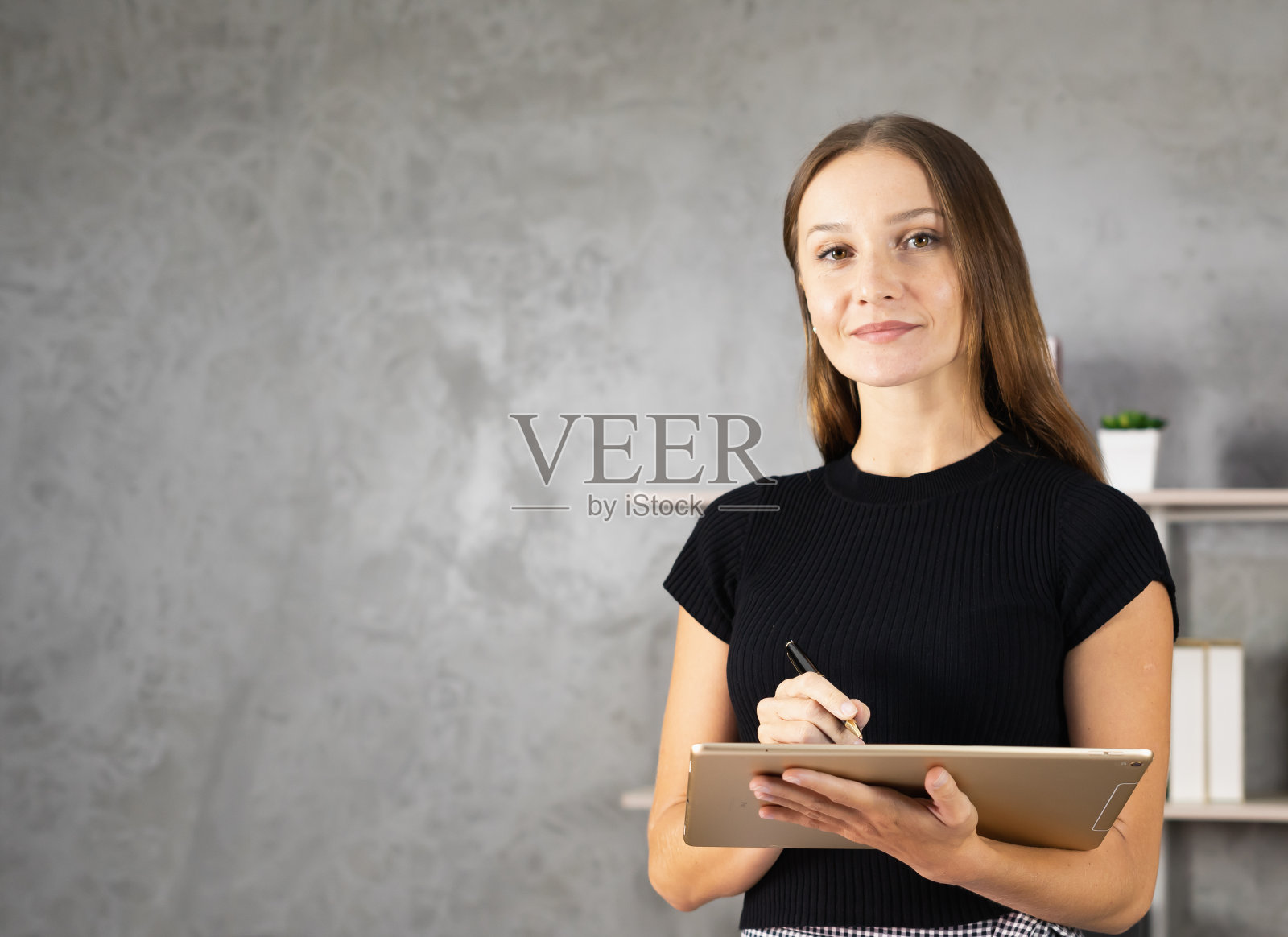 漂亮的白人妇女的肖像看着相机，而使用和工作的平板电脑附近的书架拷贝空间在背景。漂亮的白种人女人在家里放松工作照片摄影图片