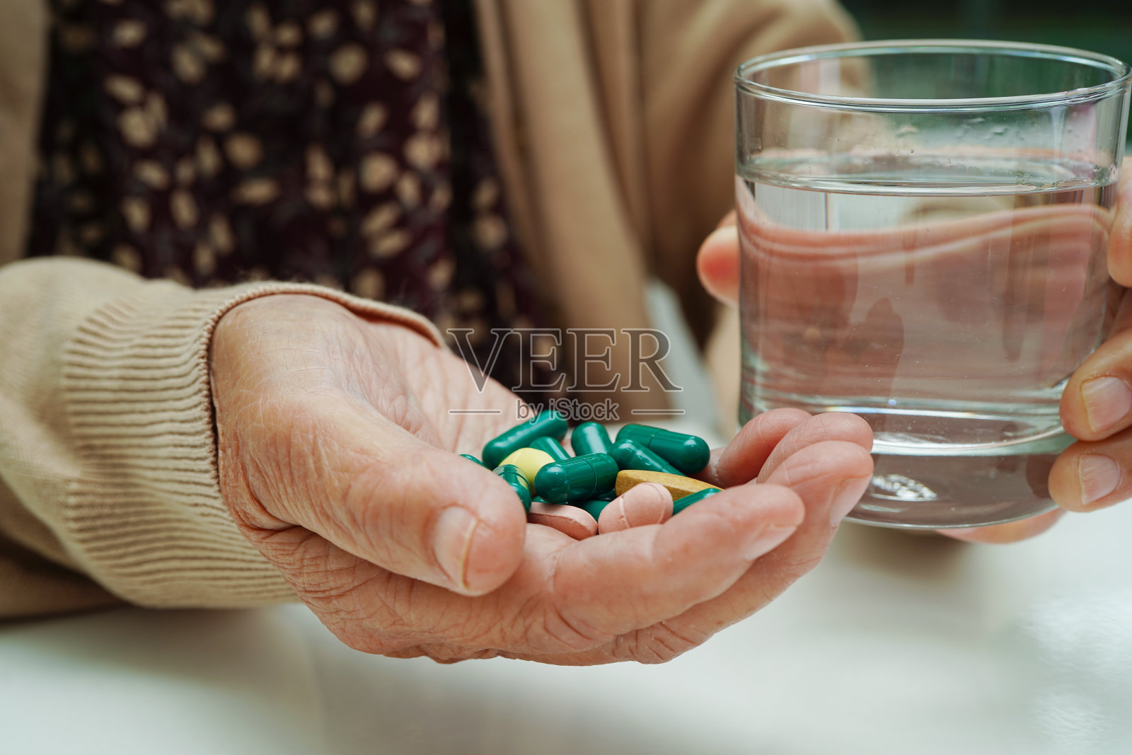 亚洲老年妇女手持药丸，药水装在玻璃中，健康医疗理念强烈。照片摄影图片
