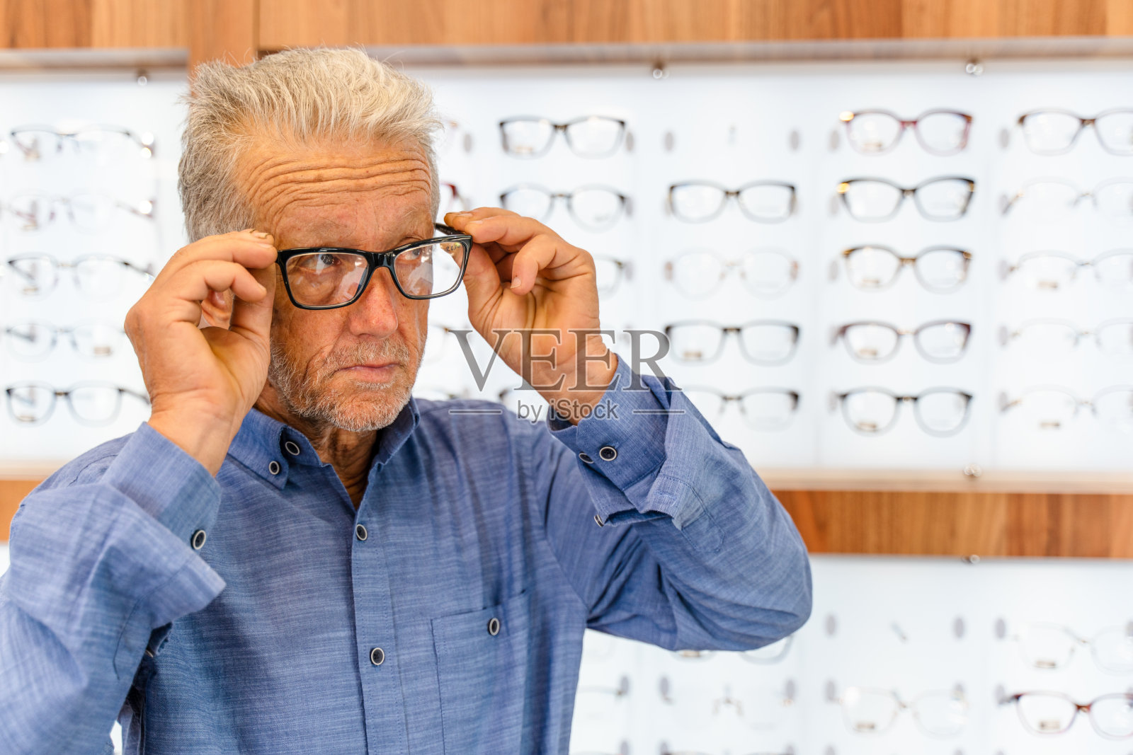 在眼镜店对着镜子试戴眼镜的年长男人照片摄影图片