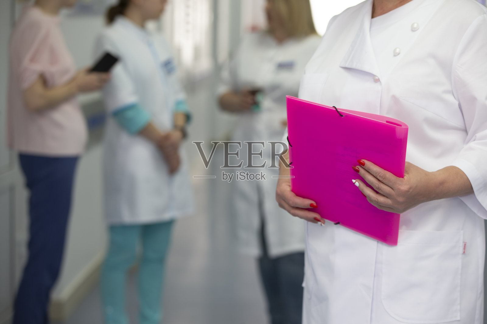 在模糊的医院走廊背景下，医生的手拿着一个文件夹。照片摄影图片