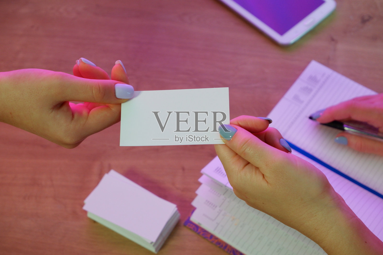 一位女士给一位客户一张名片。背景中的记事本和平板电脑放在一张木制的办公桌上。照片摄影图片