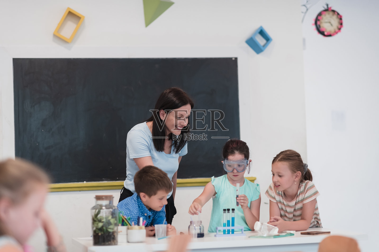 小学科学课堂:热情的老师向不同的孩子们讲解化学，小男孩在烧杯中混合化学物质。孩子有兴趣地学习照片摄影图片
