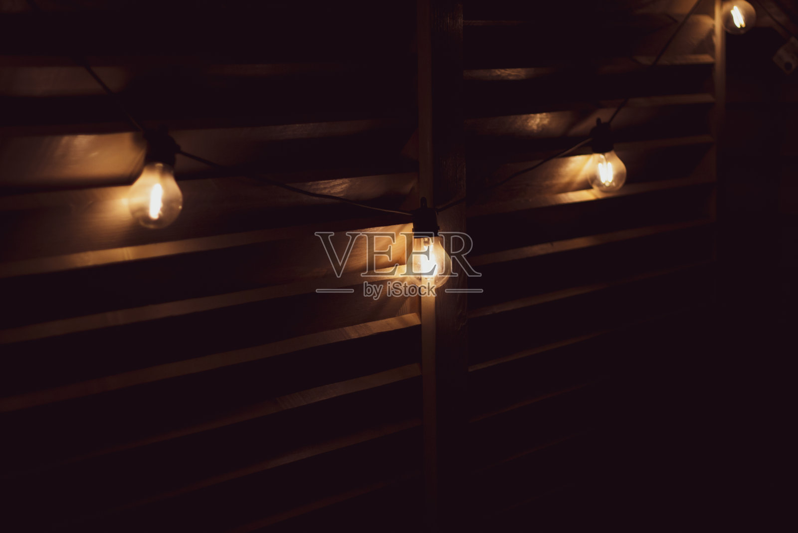 花冠在夜天井。灯泡花环。夜晚的灯光。时尚庭院装饰。在黑暗中发光的灯泡。照片摄影图片