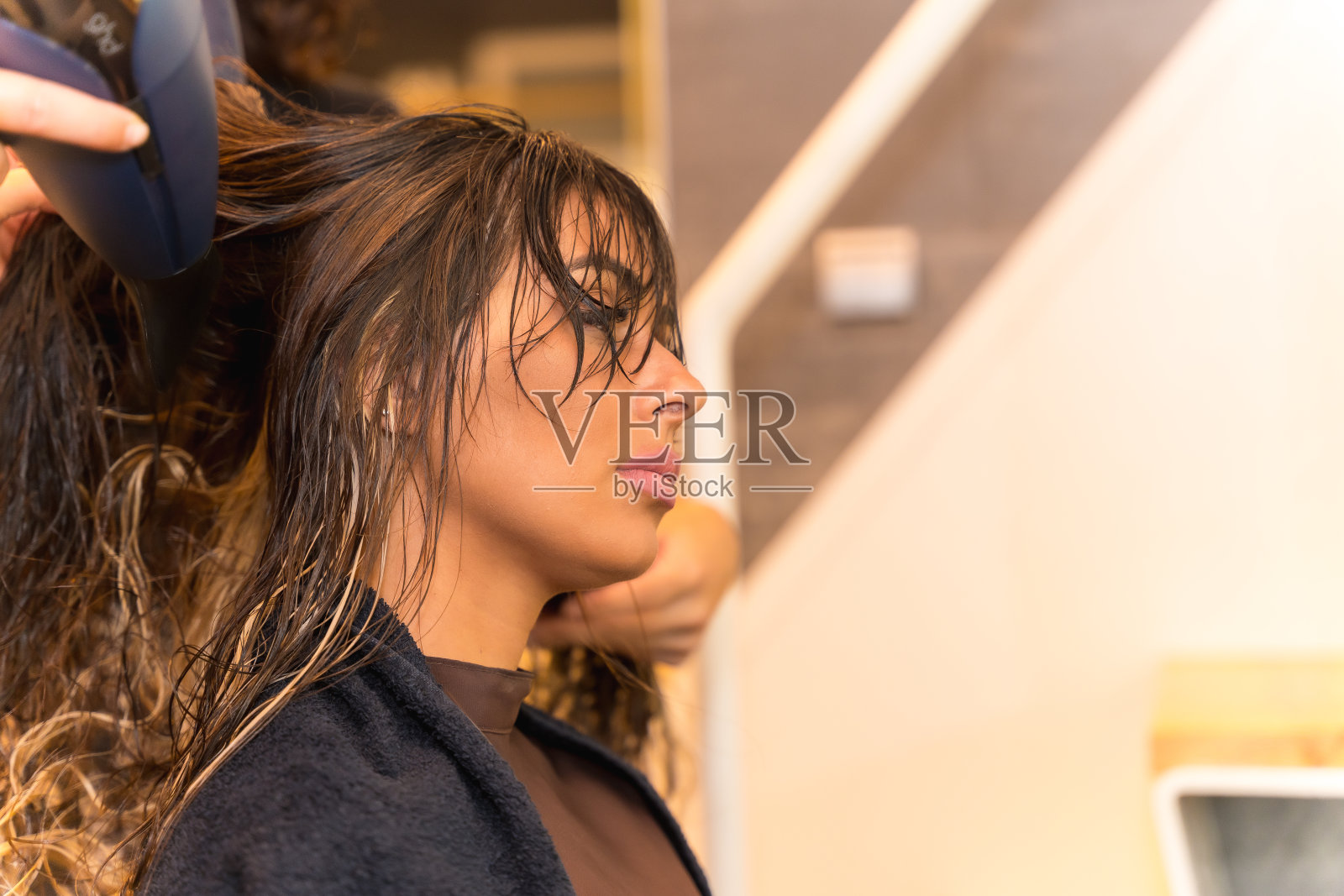 一个深色头发的女人坐在美容院用吹风机吹干她的头发照片摄影图片