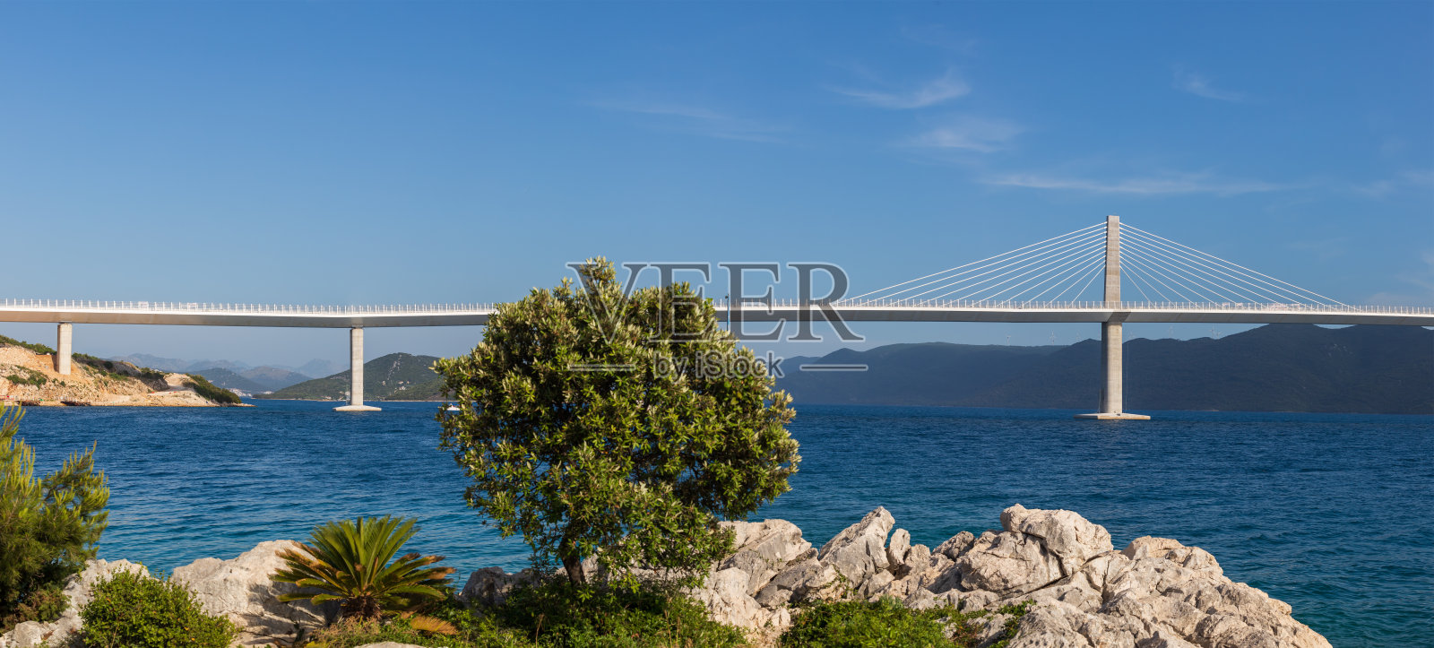 克罗地亚佩列沙茨海上的一座美丽的现代化大桥。前景是房屋，背景是佩列沙克山脉照片摄影图片