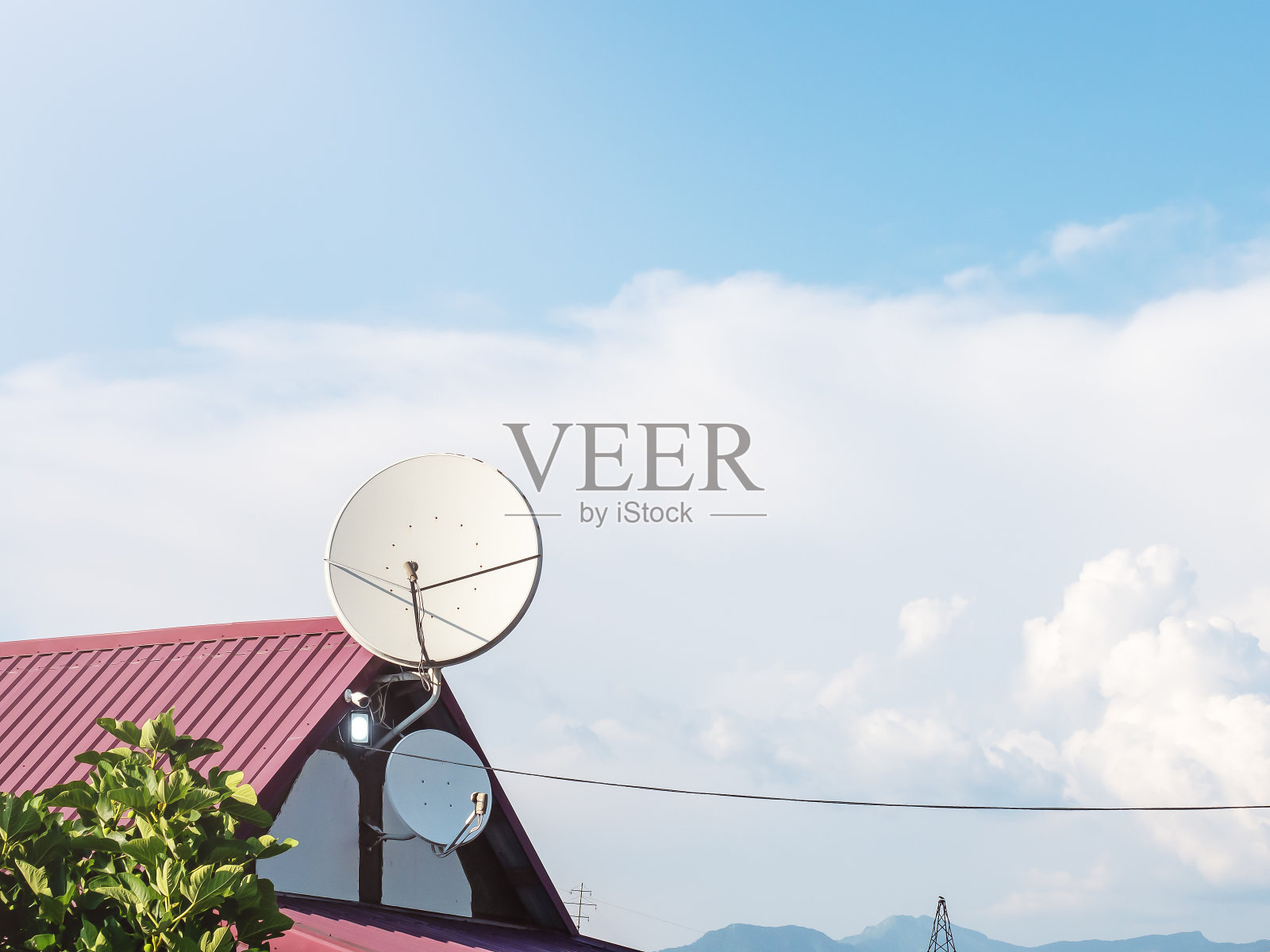 屋顶上的圆形天线。蓝色多云的天空映衬着一栋私人住宅顶部的两根白色卫星电视天线照片摄影图片