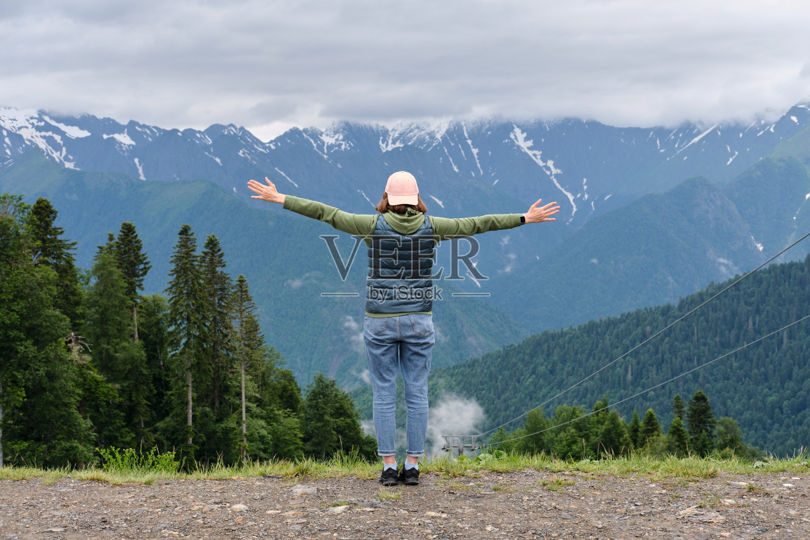 快乐女人的背影举起她的手，享受山峰的景色。照片摄影图片