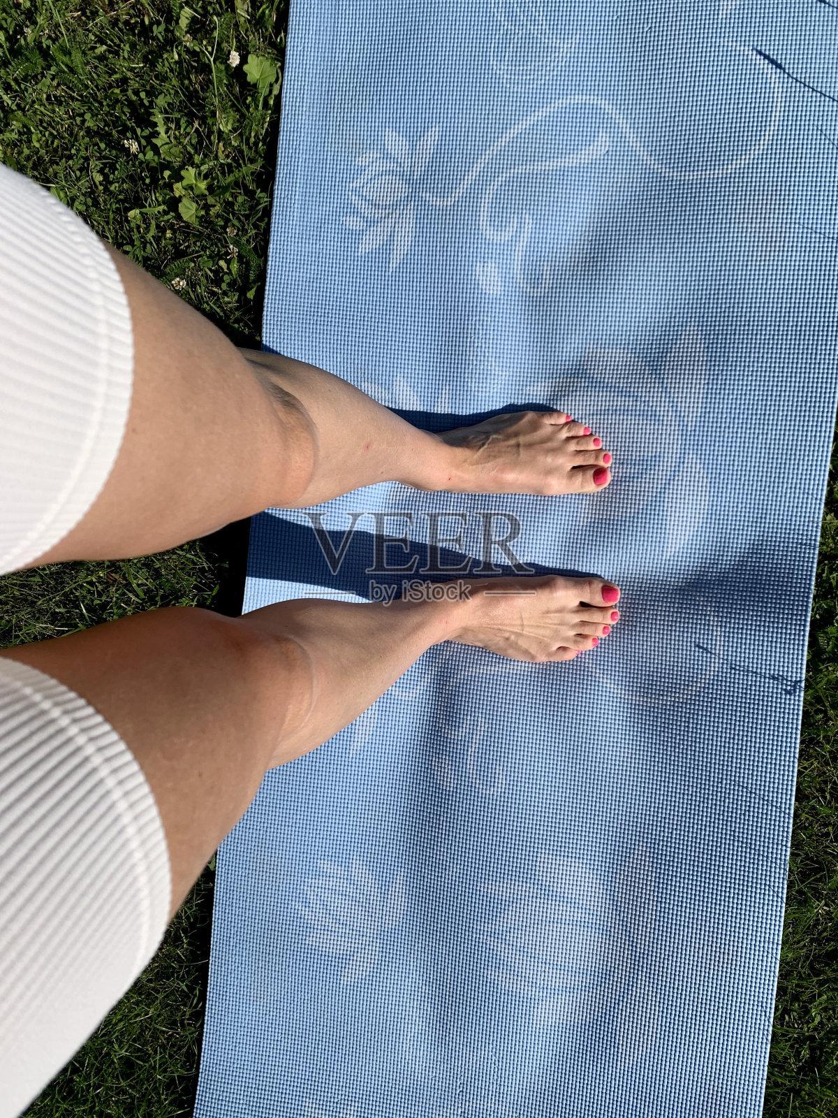 运动垫上的女性腿。健身时间。外面的草地上照片摄影图片