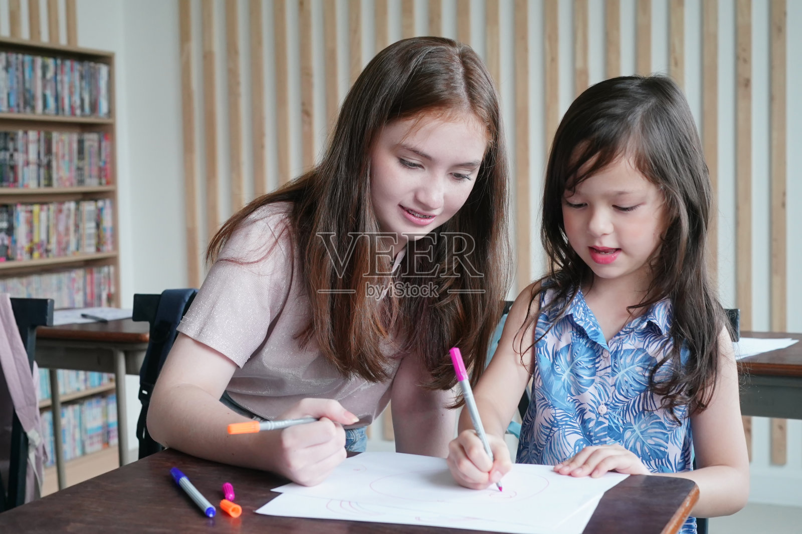 学前班女孩孩子在教室的桌子上用彩色铅笔在白纸上画画照片摄影图片