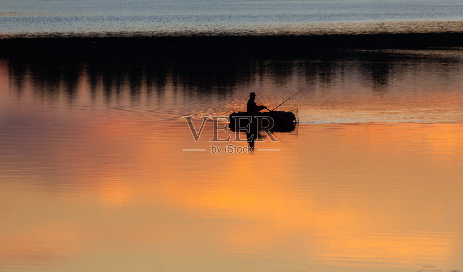 日落时分湖面上小船上渔夫的剪影照片摄影图片