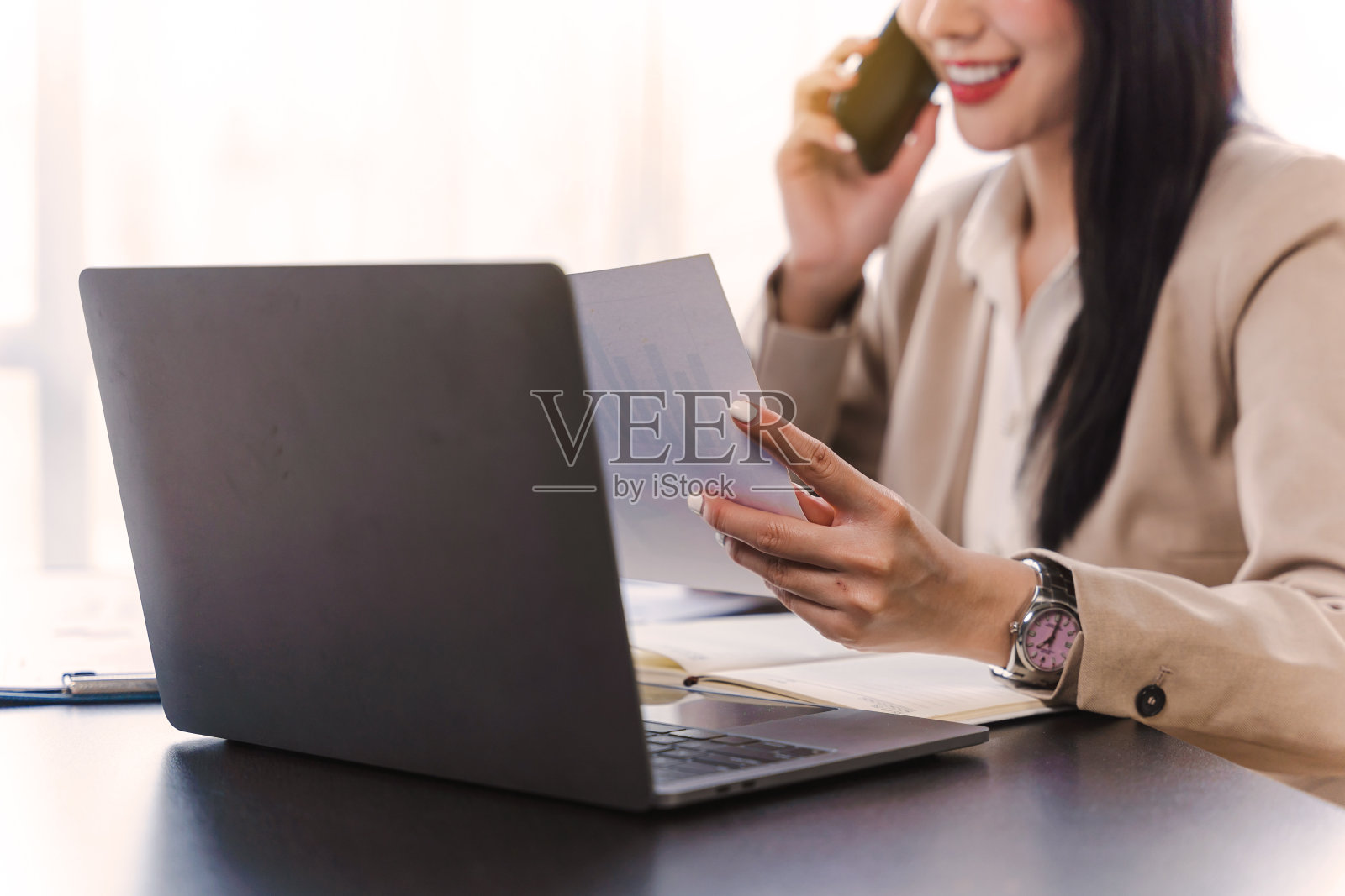 亚洲商务女性喜欢在办公室桌上放着笔记本电脑和平板电脑煲电话粥。照片摄影图片