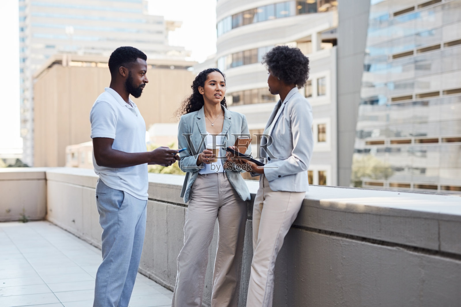 商务人士工作时在大楼阳台上交谈。在现代工作场所的公司露台上开会的同事们。同事们一起头脑风暴和讨论一个项目照片摄影图片