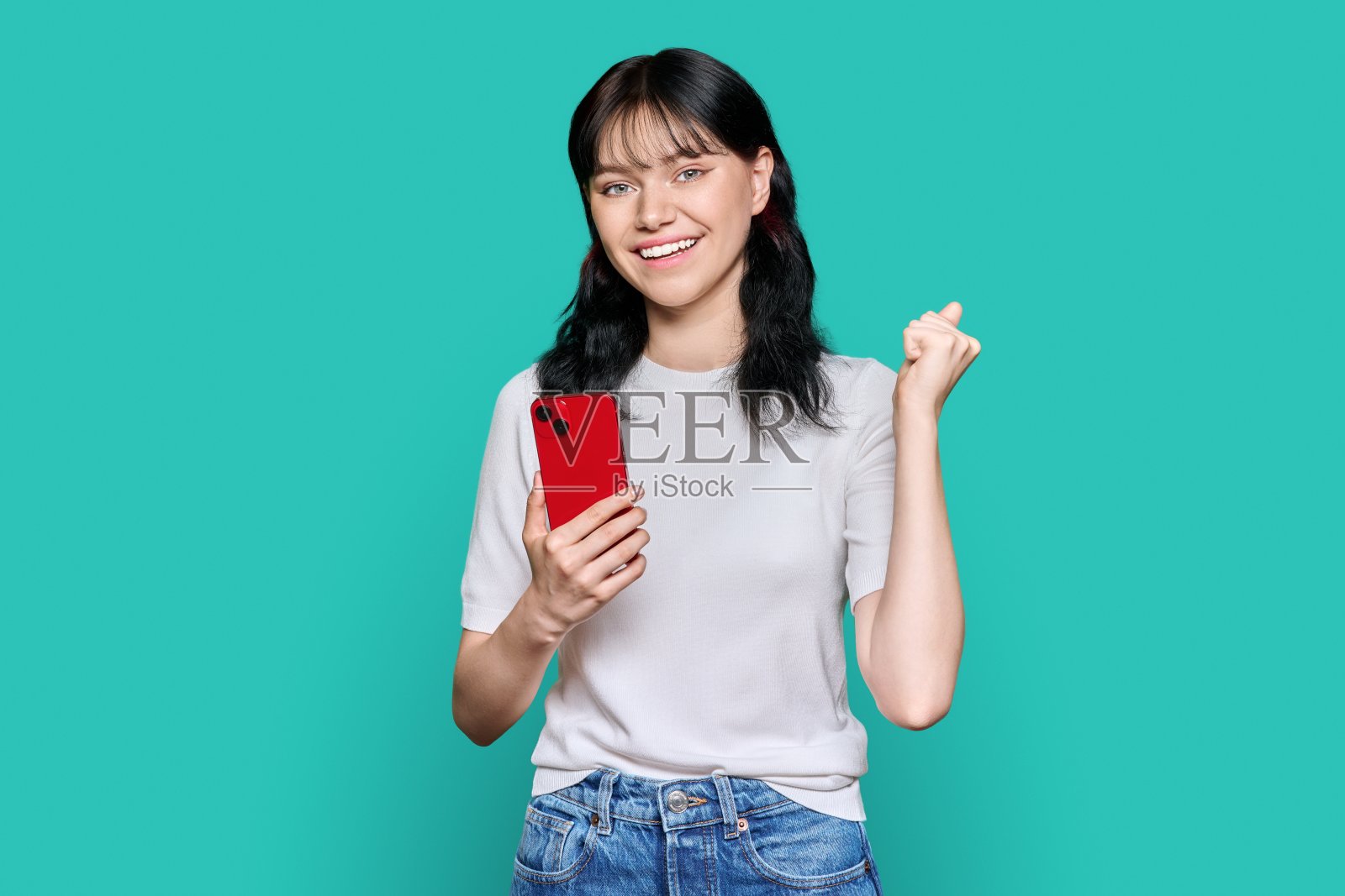 肖像快乐的女孩与智能手机举起她的拳头，是的符号照片摄影图片