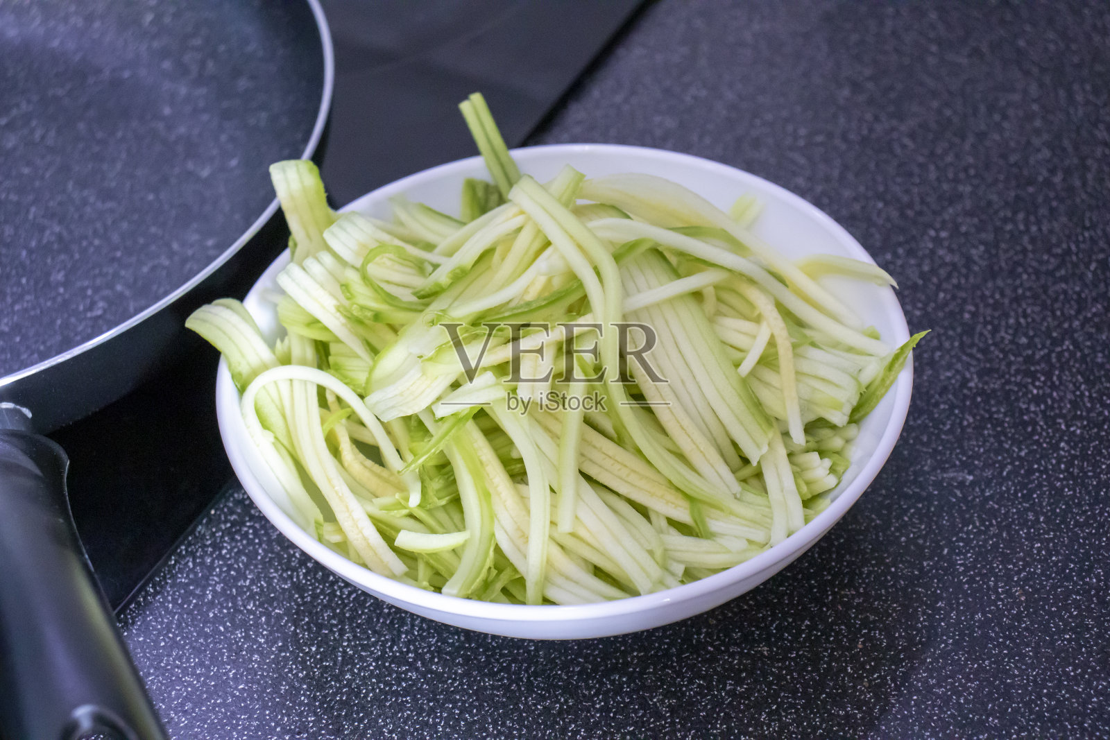 黑桌子上的煎锅旁边的盘子里有西葫芦做的意大利面照片摄影图片