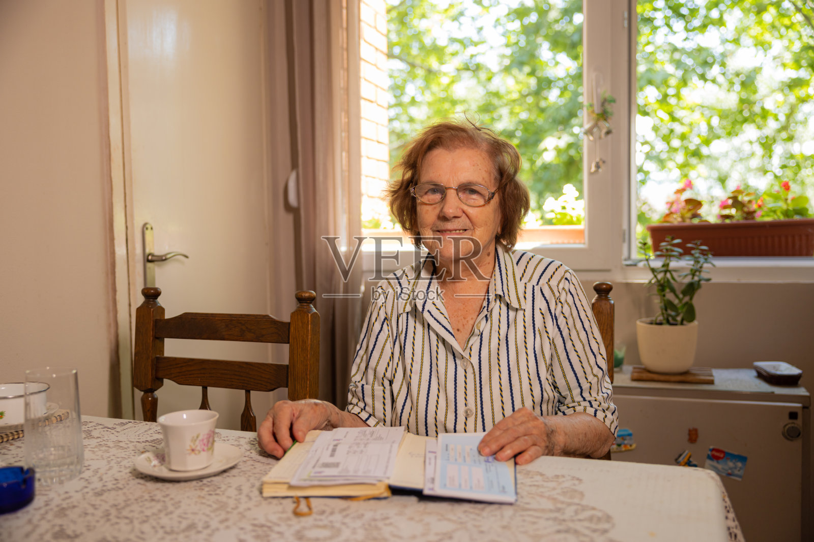 开朗的老年高加索妇女的肖像，94岁，坐在桌子和阅读一本书照片摄影图片