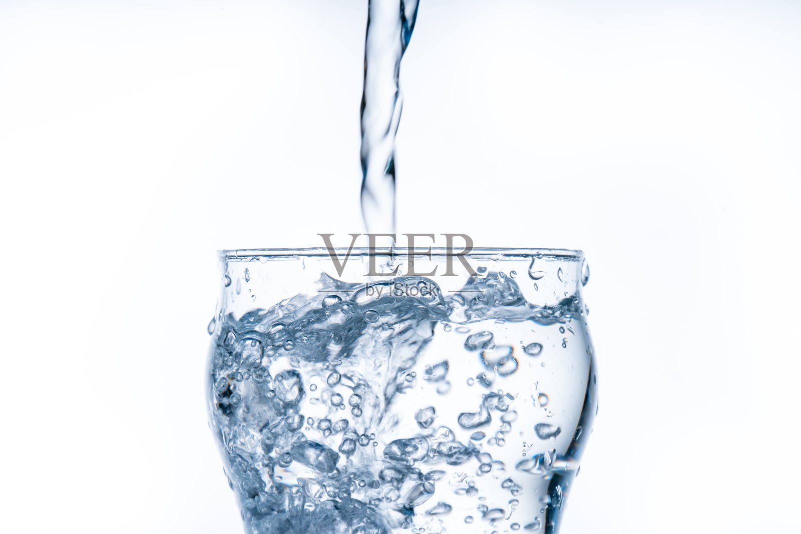 一块冰块掉进了水杯里。水从透明的玻璃上飞溅出来。新鲜的概念照片摄影图片