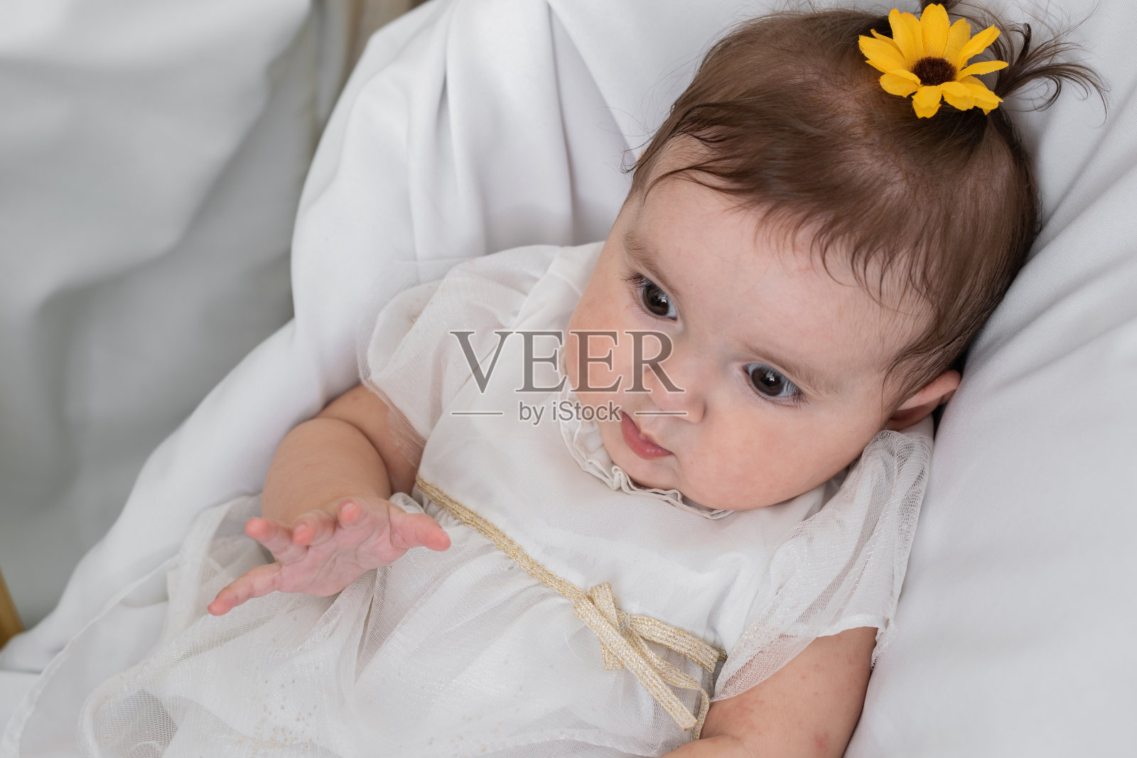 一个美丽的婴儿躺在婴儿床上，躺在白色的床单上，头上戴着一朵美丽的人造花。婴儿和母亲的概念。照片摄影图片