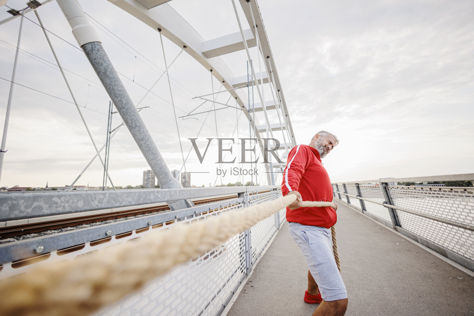 强壮成熟的成年男子在户外用战绳锻炼。肌肉发达的运动员在户外用绳索进行交叉远足。意志坚定的家伙在进行体能训练时使用战斗绳。照片摄影图片