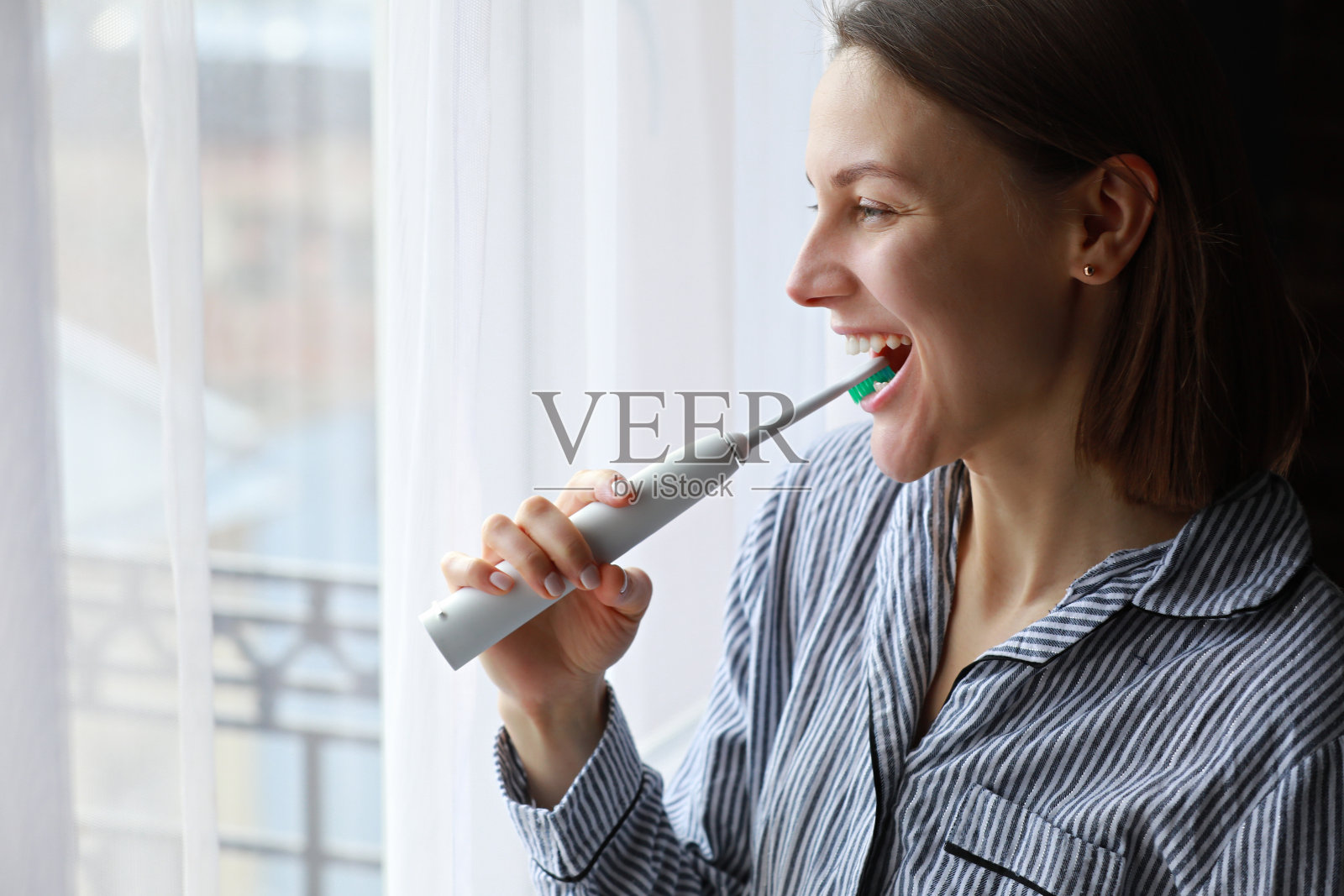 这个女孩用电刷刷牙。一个年轻漂亮的女孩在镜子前用电动牙刷刷牙。口腔卫生。照片摄影图片