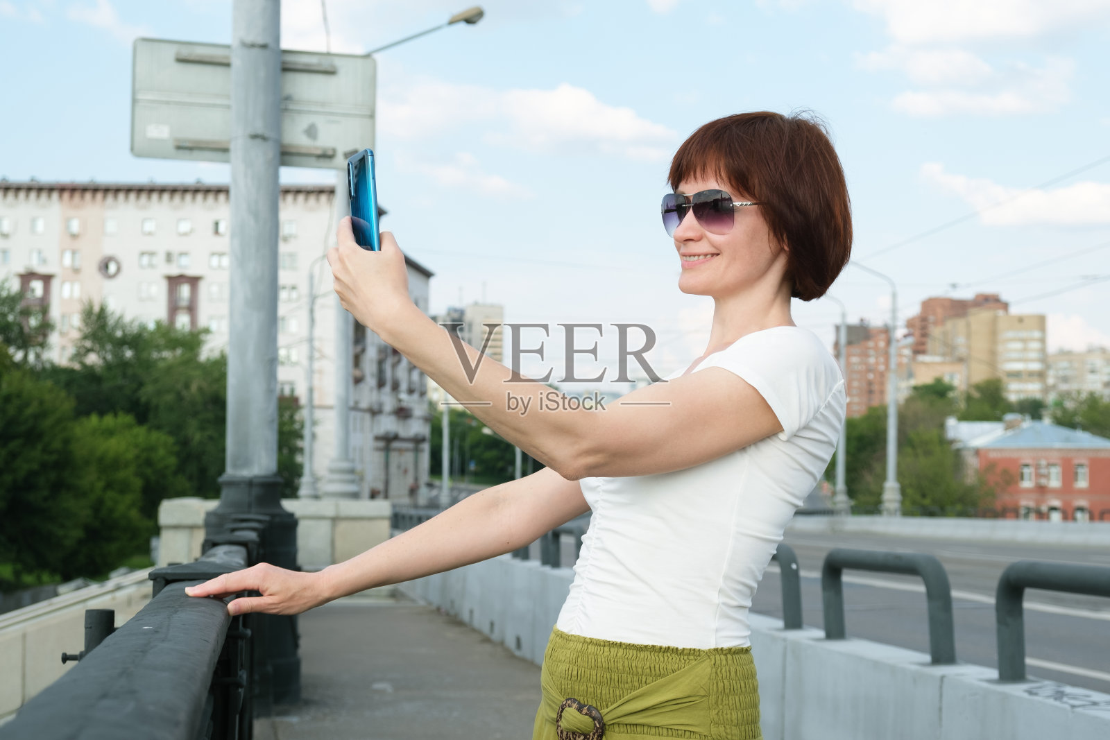 戴着墨镜的女人微笑着对着他的智能手机屏幕，在他伸手给自己的手机拍照照片摄影图片