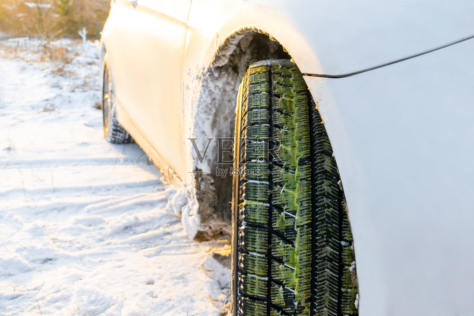 冬天的乡村道路上，白色的轿车轮胎和绿色的草的车轮的特写，自然景观覆盖在雪在夕阳下照片摄影图片