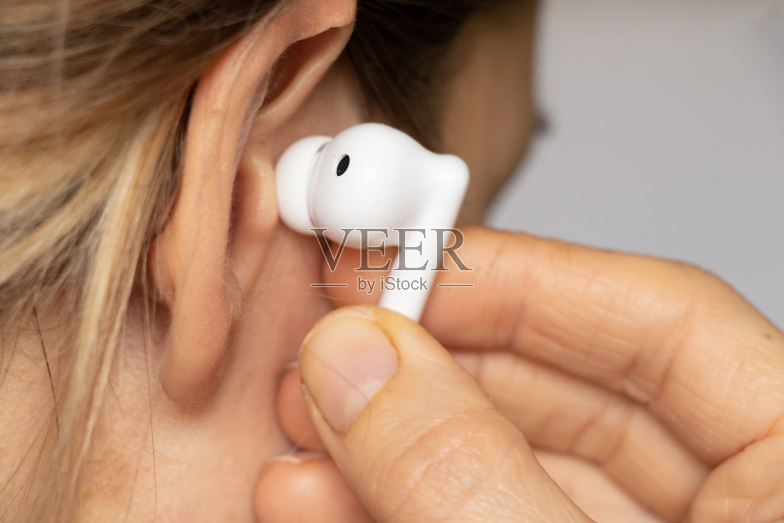 无线白色耳机在女孩耳边特写，戴着耳机听音乐，无线耳机照片摄影图片