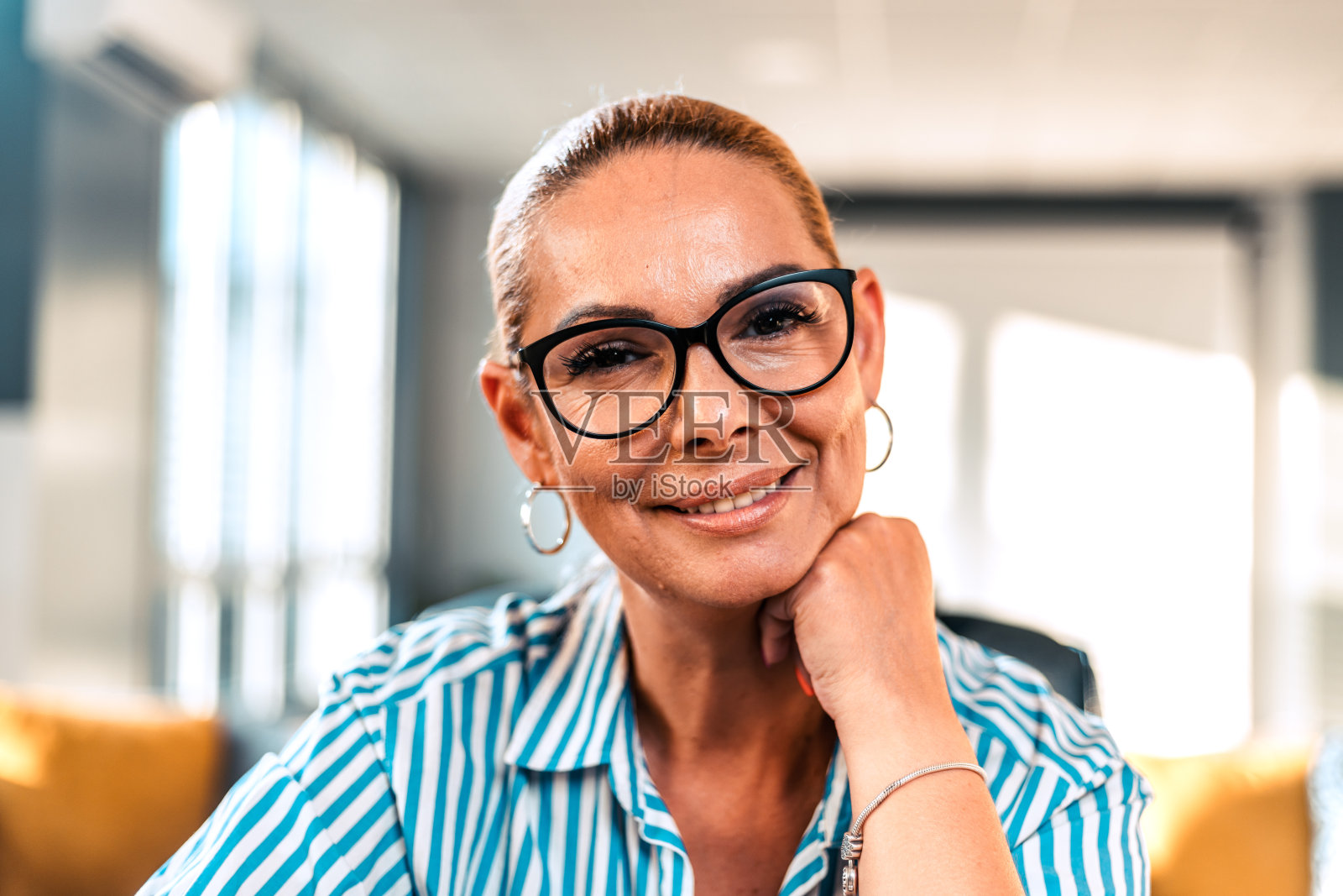 成熟微笑的女人看着相机的肖像。快乐的女人坐在创意办公室里。办公室里有复印空间的成功女商人。照片摄影图片