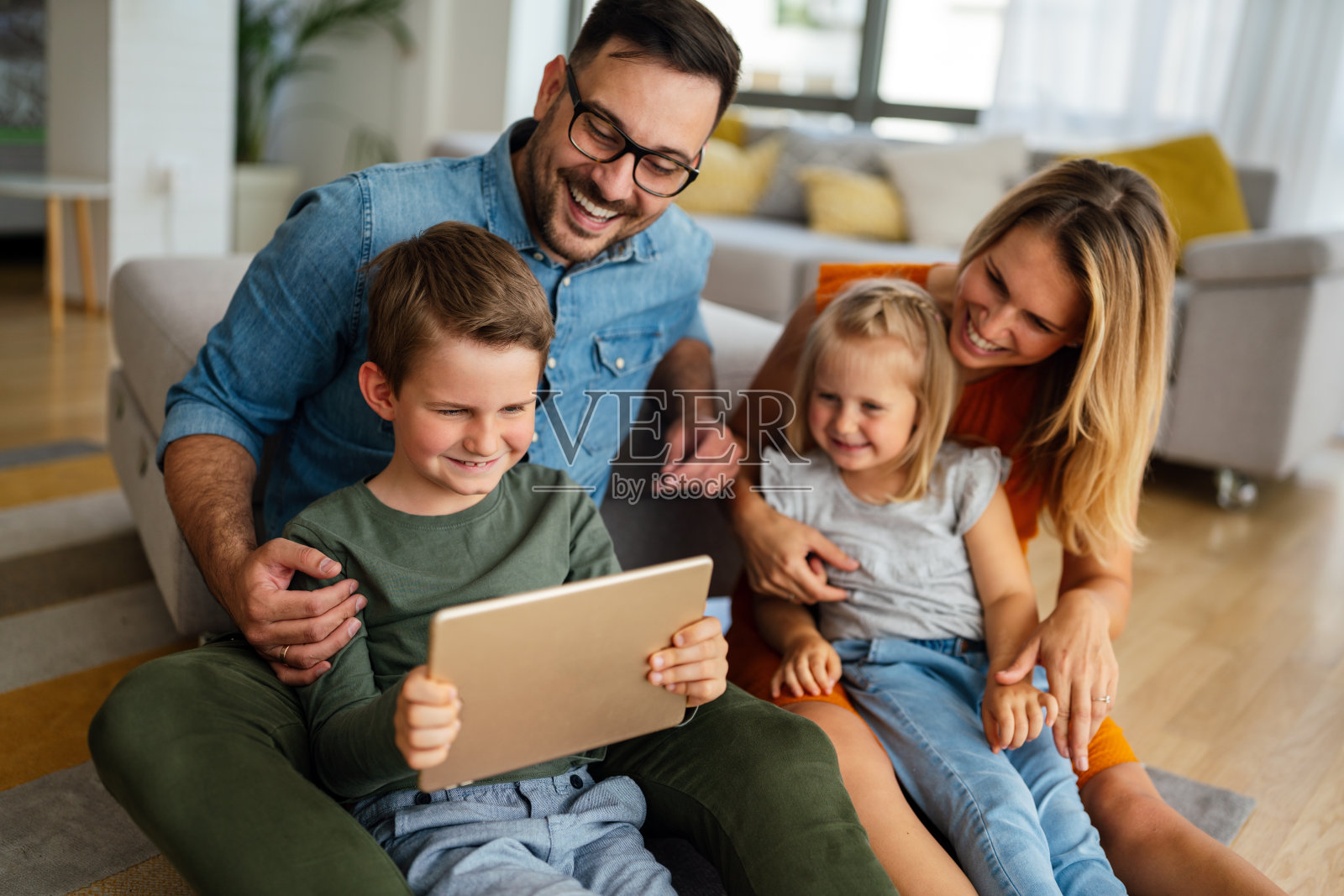 快乐的年轻家庭在家里玩得很开心。孩子使用数码设备的父母。照片摄影图片