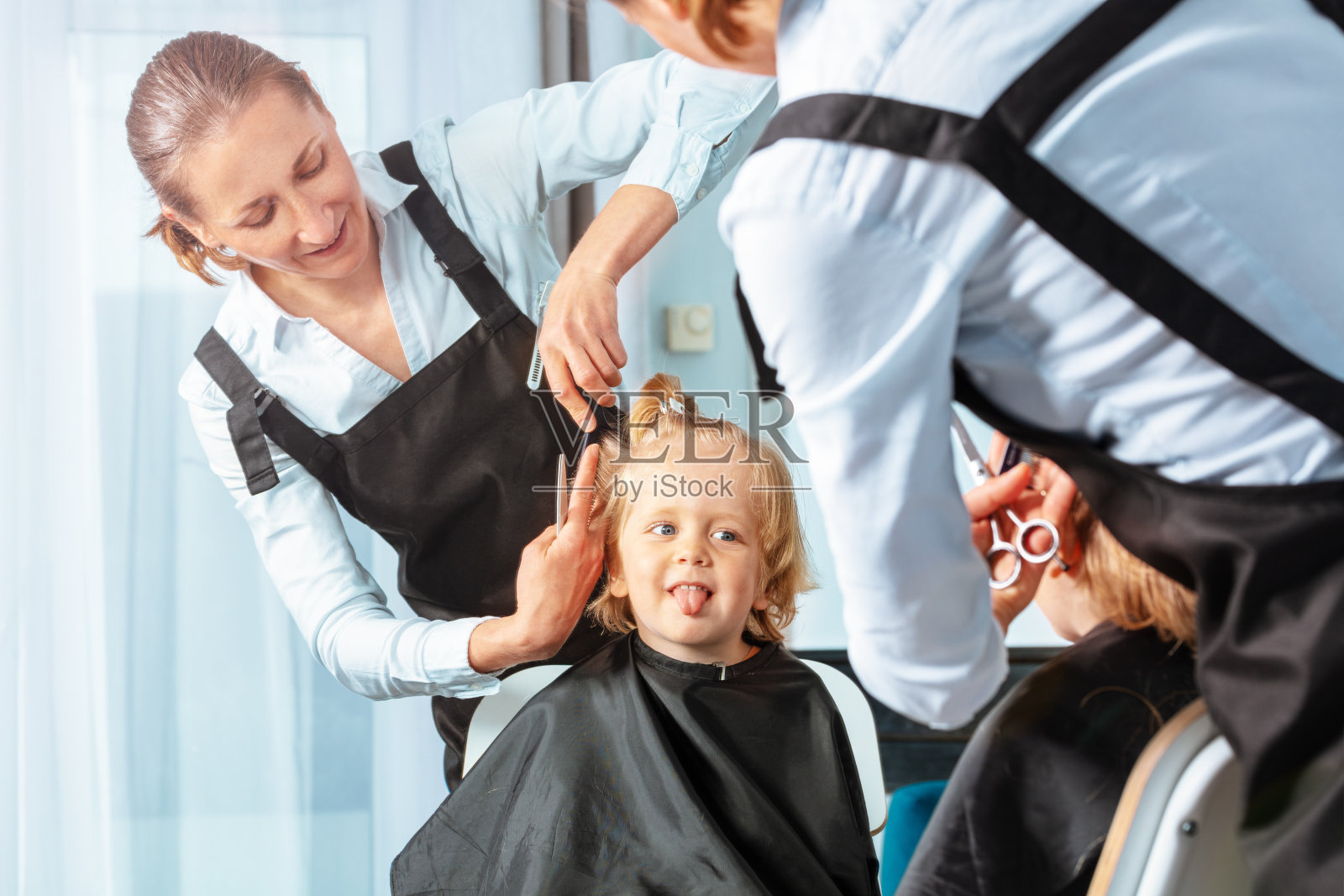 理发师给女人理发时，男孩伸出舌头照片摄影图片