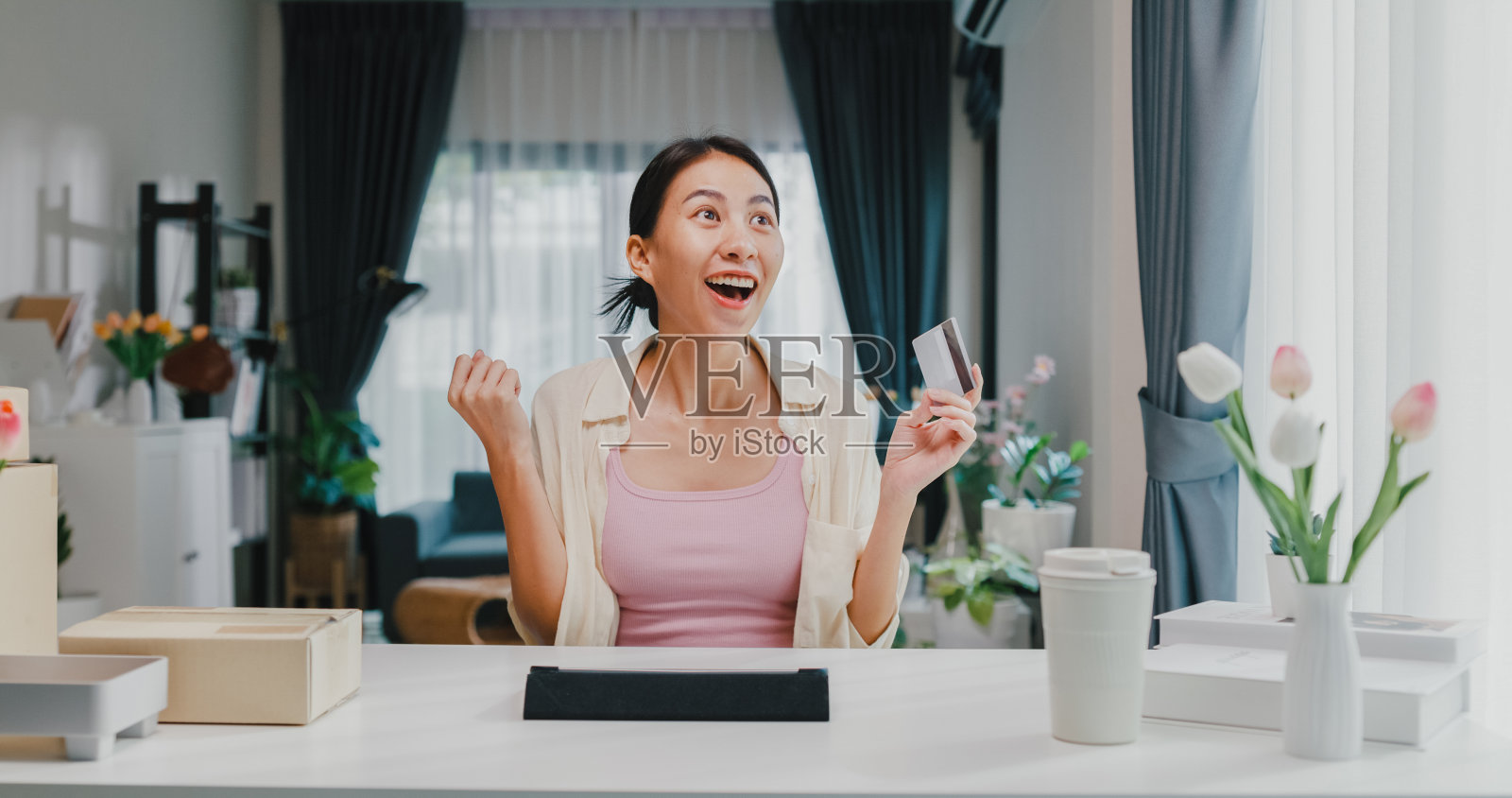 年轻的亚洲女女孩穿着休闲坐在书桌前与数字平板电脑和信用卡感到兴奋和快乐，在网上购物成功支付在客厅在家里。照片摄影图片