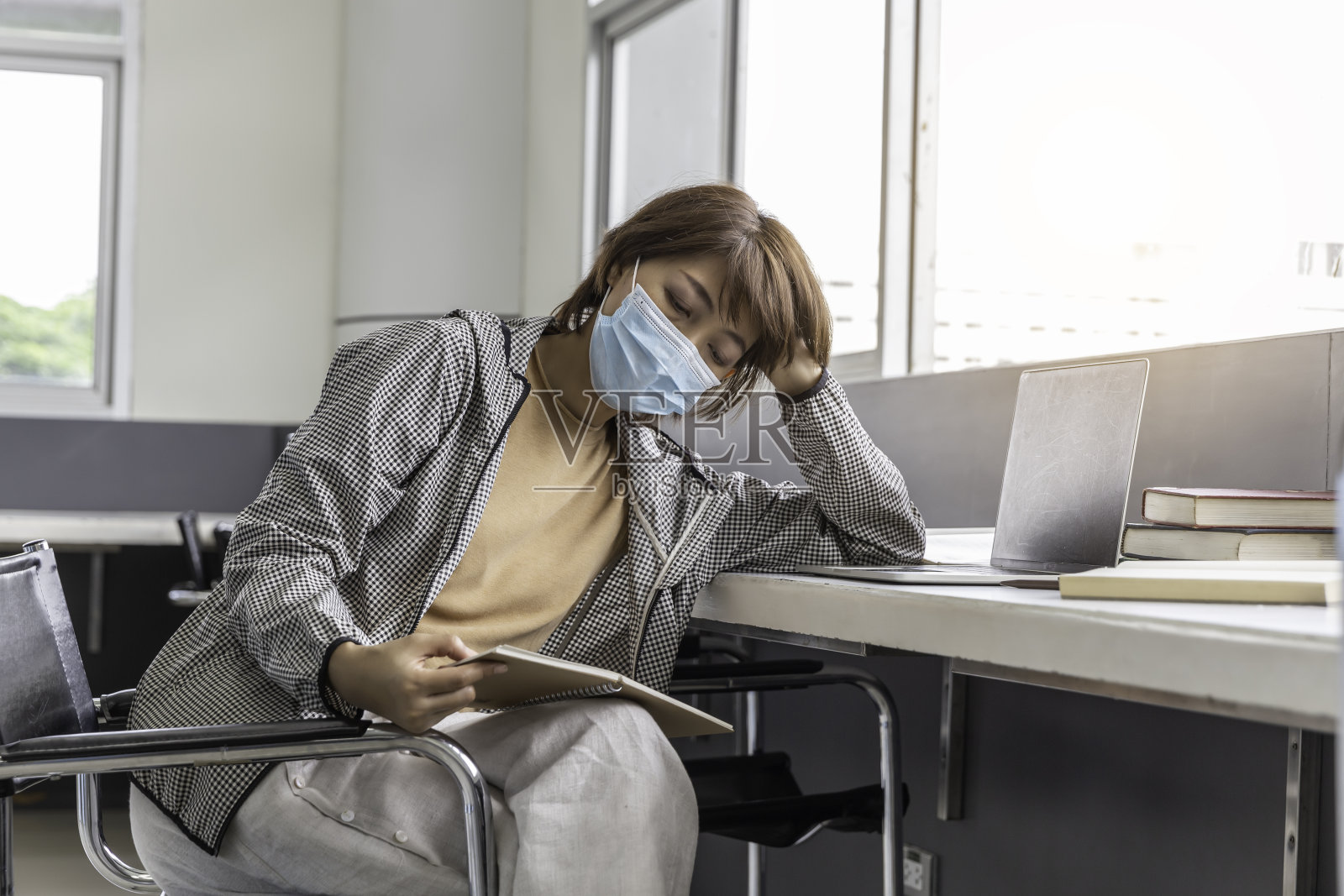 美丽的女人戴着口罩在图书馆看书。照片摄影图片